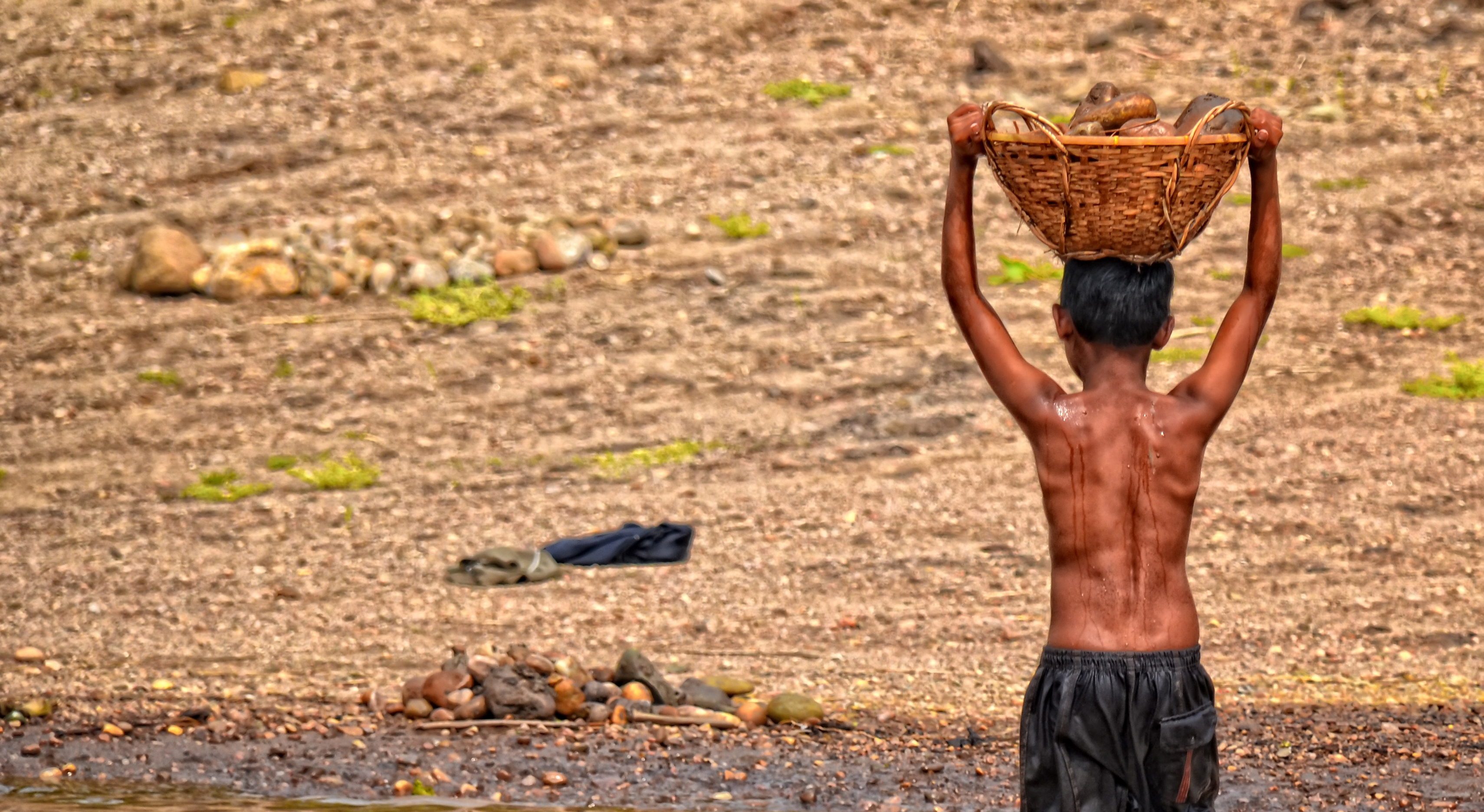 Ein Junge in Bangladesch transportiert einen mit Steinen gefüllten Korb. 