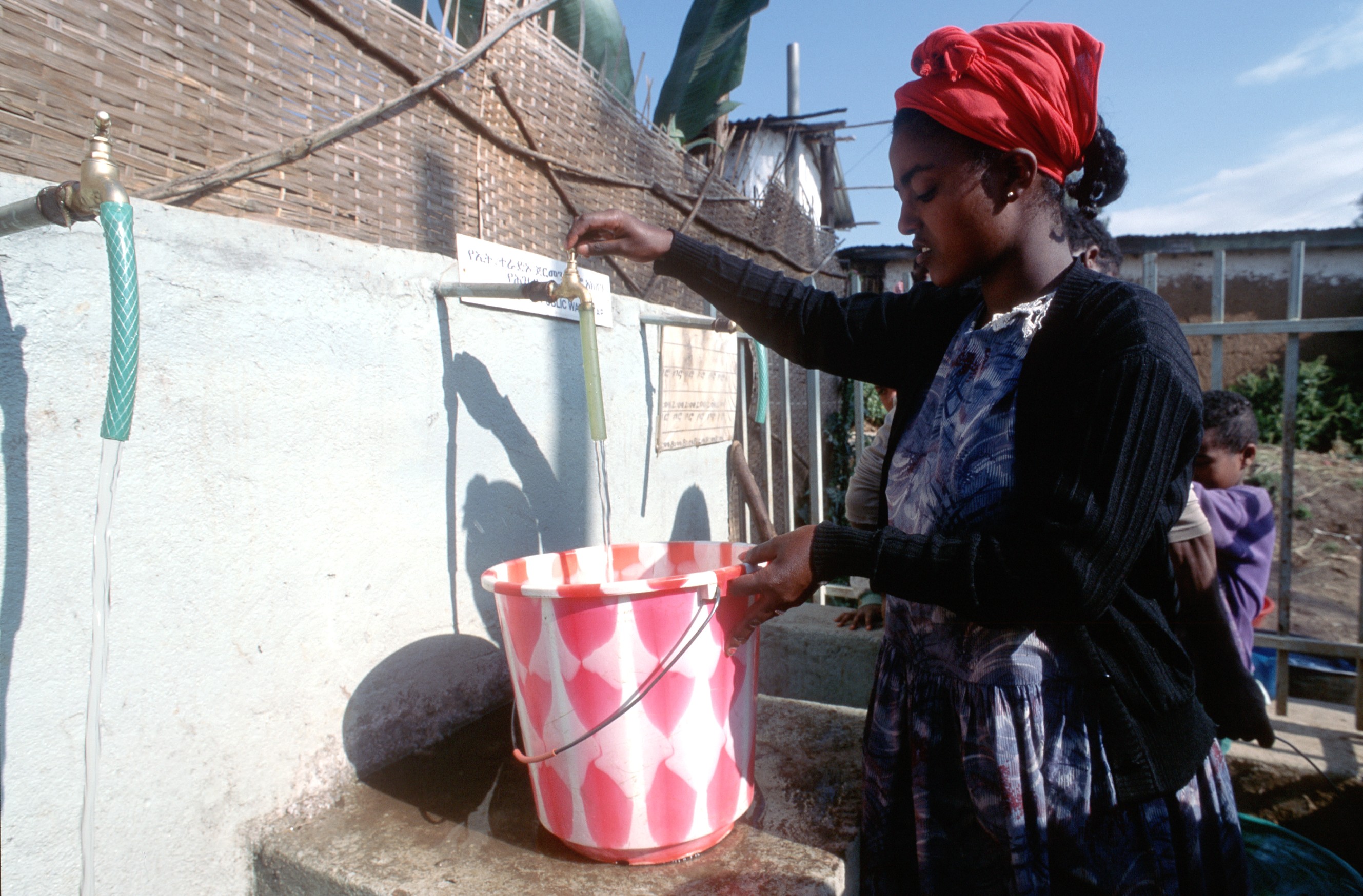 An einer Trinkwasserstelle füllt eine Frau ihren Eimer mit Wasser