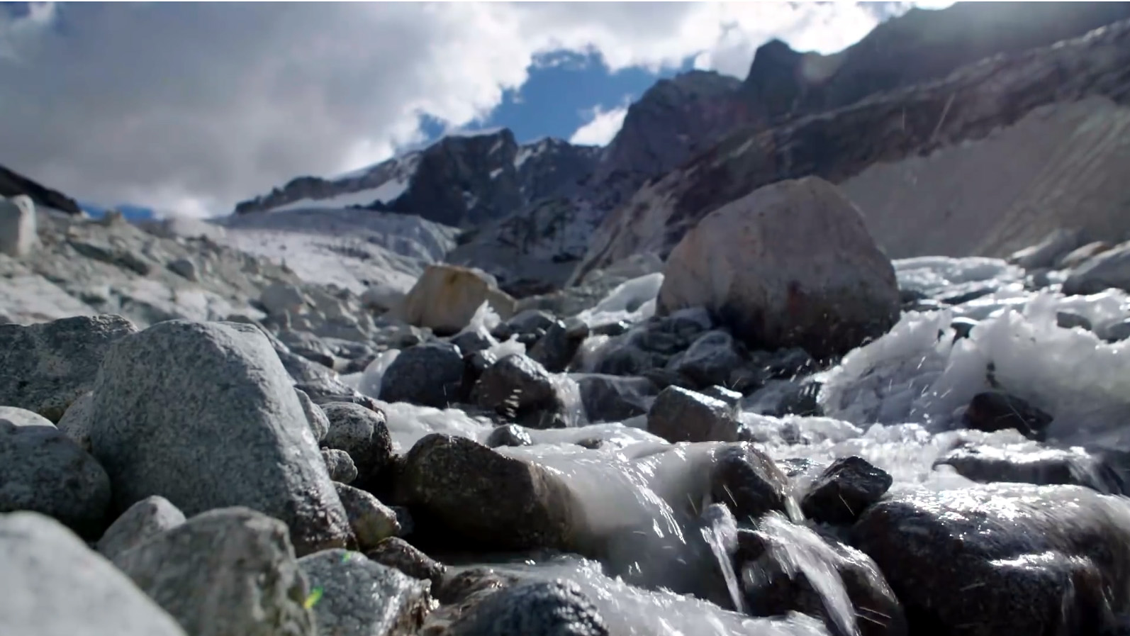 Standbild aus dem BMZ-Video "Gletscherschmelze in Bolivien". Ein vereister Bach fließt vor dem Hintergrund eines verschneiten Hochgebirges.