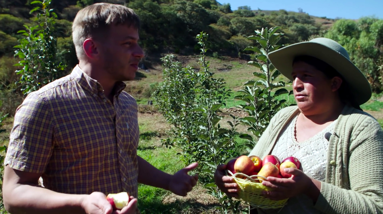 Standbild aus dem BMZ-Video "Der Klimawandel und die Apfelernte in Bolivien". Der Schauspieler Tom Wlaschiha unterhält sich mit einer bolivianischen Bäuerin, im Hintergrund eine Apfelplantage.