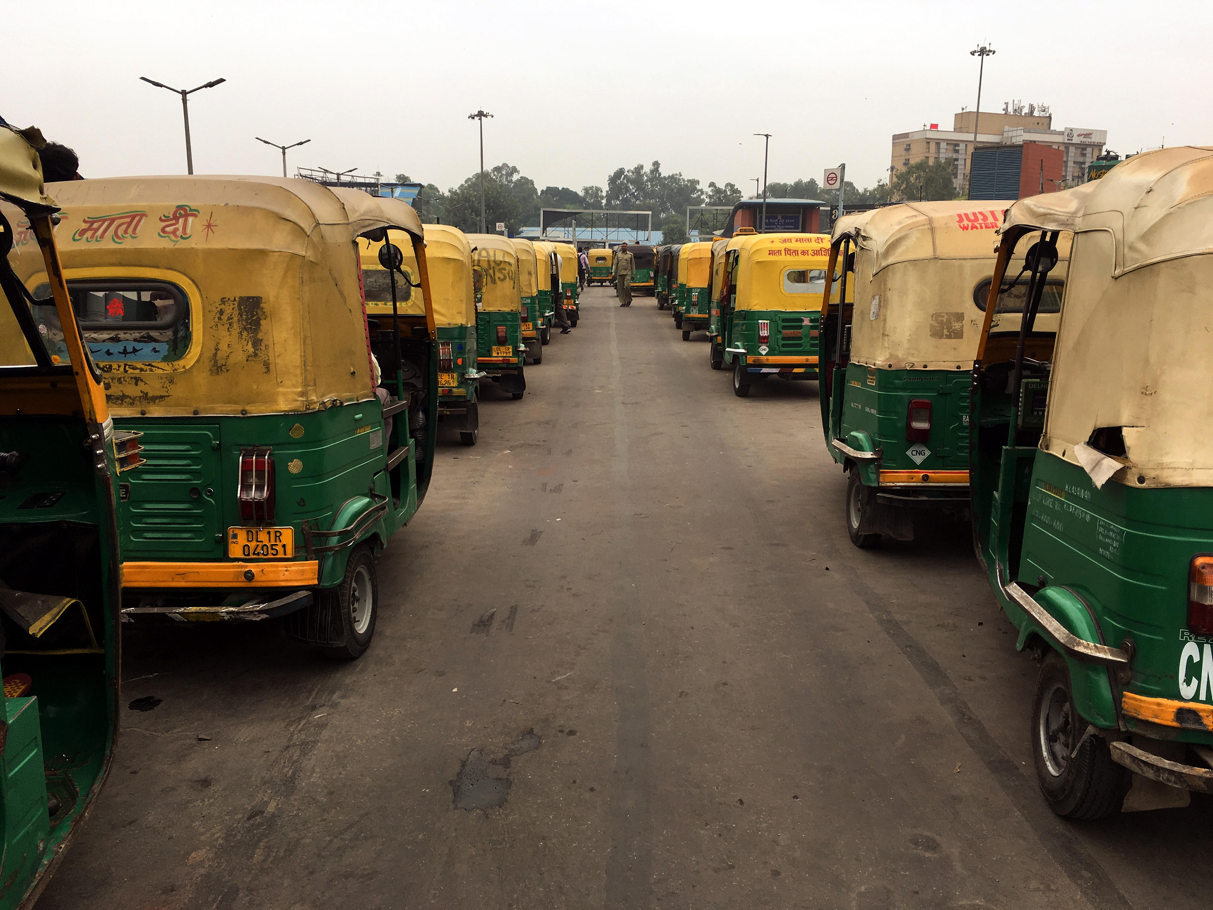 Motorrad-Taxis stehen in zwei langen Reihen nebeneinander auf einer Straße in Delhi, Indien.