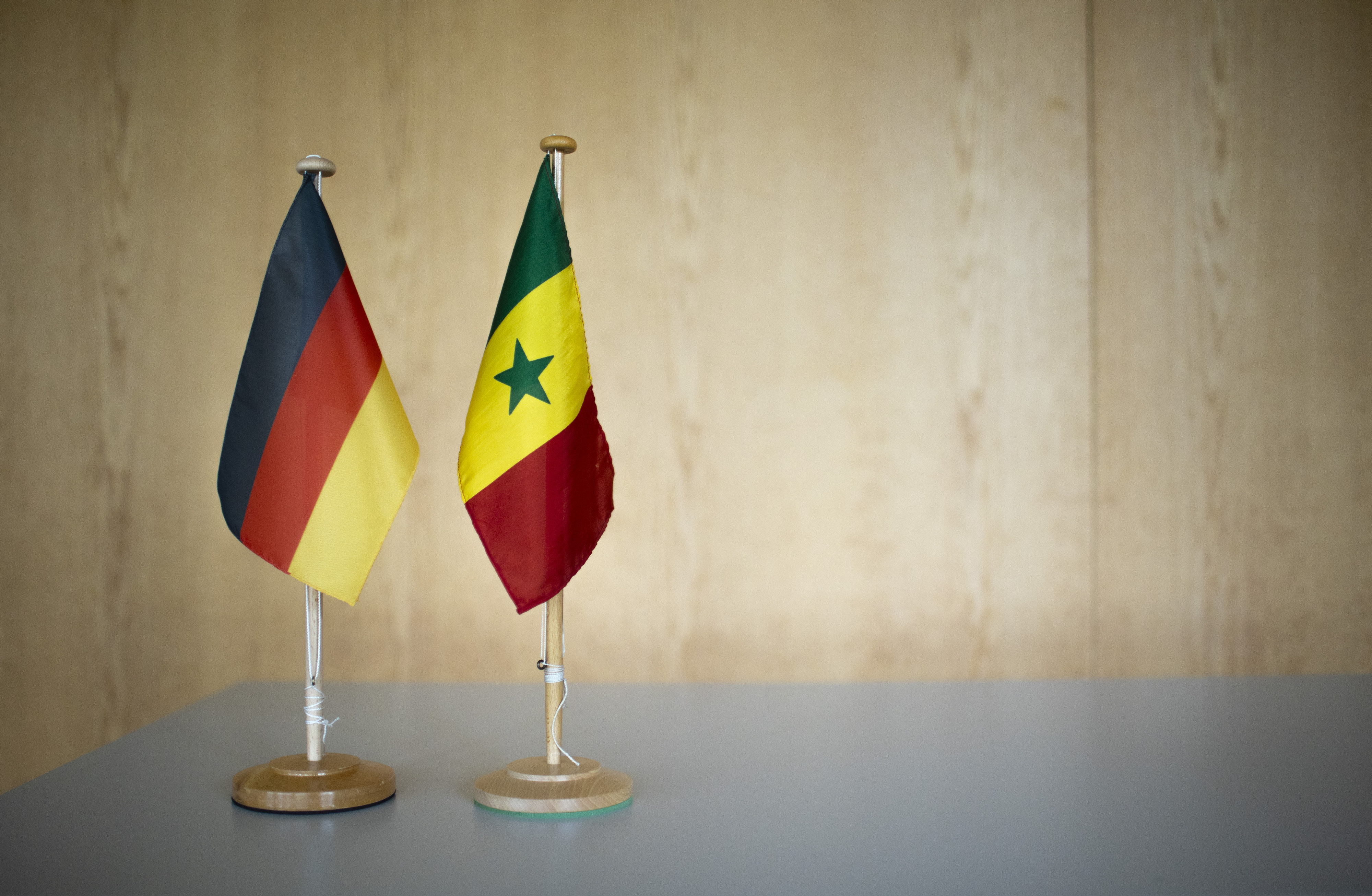 Tischflaggen von Deutschland und Senegal stehen nebeneinander auf einer Tischplatte vor einer Wand