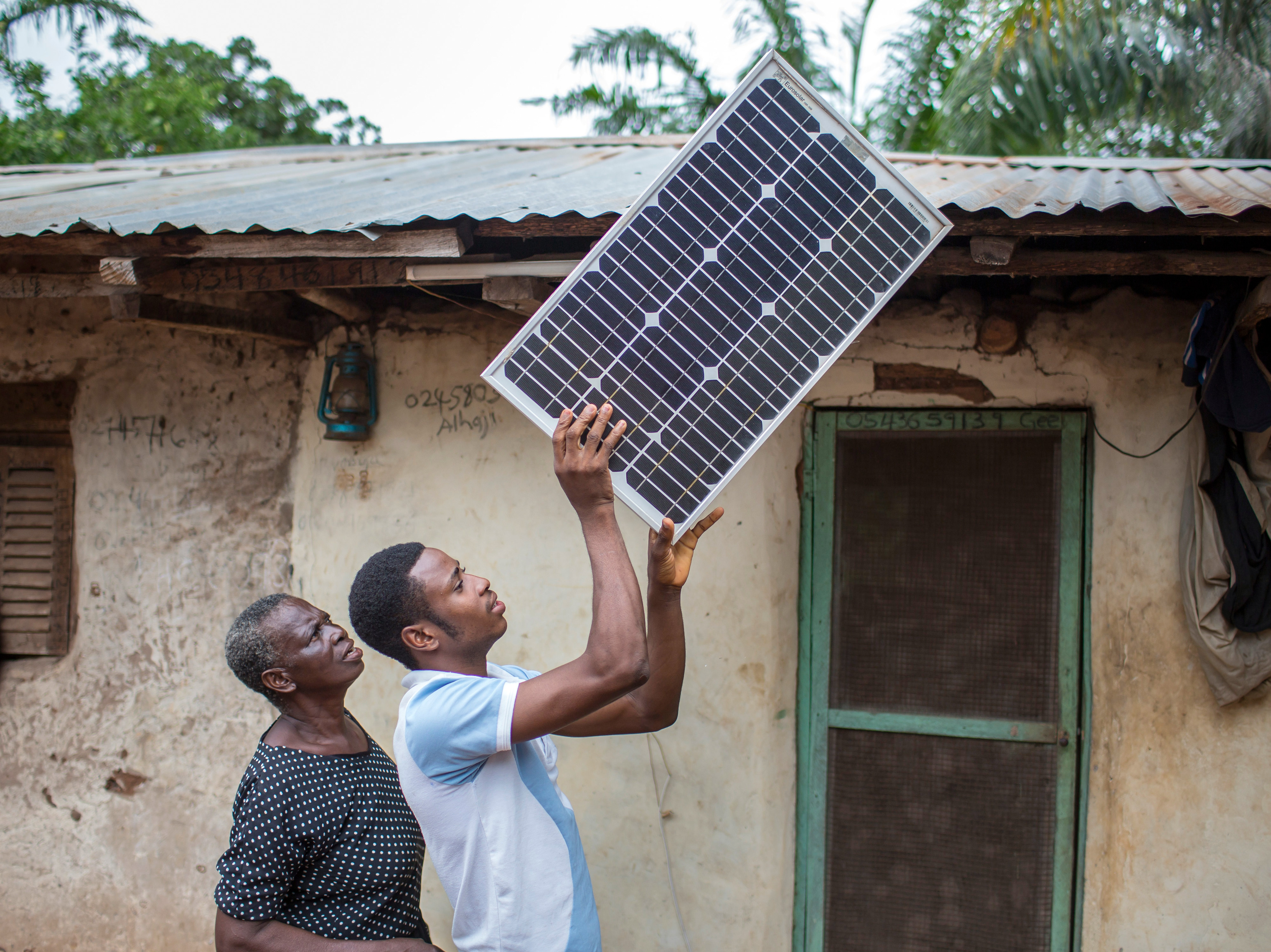 A young African farmer installs a solar panel on the roof of his house on a cashew farm.