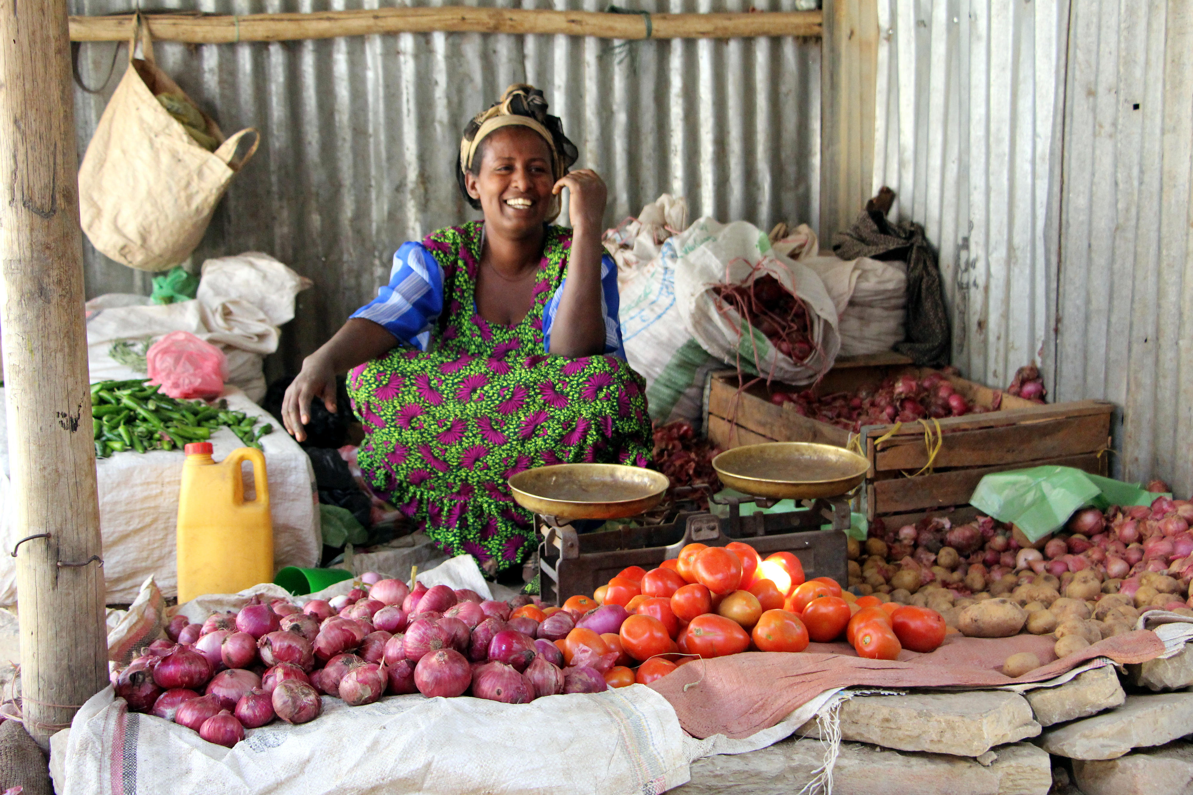 Marktstand in Mekelle, Äthiopien, mit Zwiebeln, Tomaten und Kartoffeln, die zum Kauf angeboten werden. Im Hintergrund steht eine Waage mit zwei leeren Waagschalen.