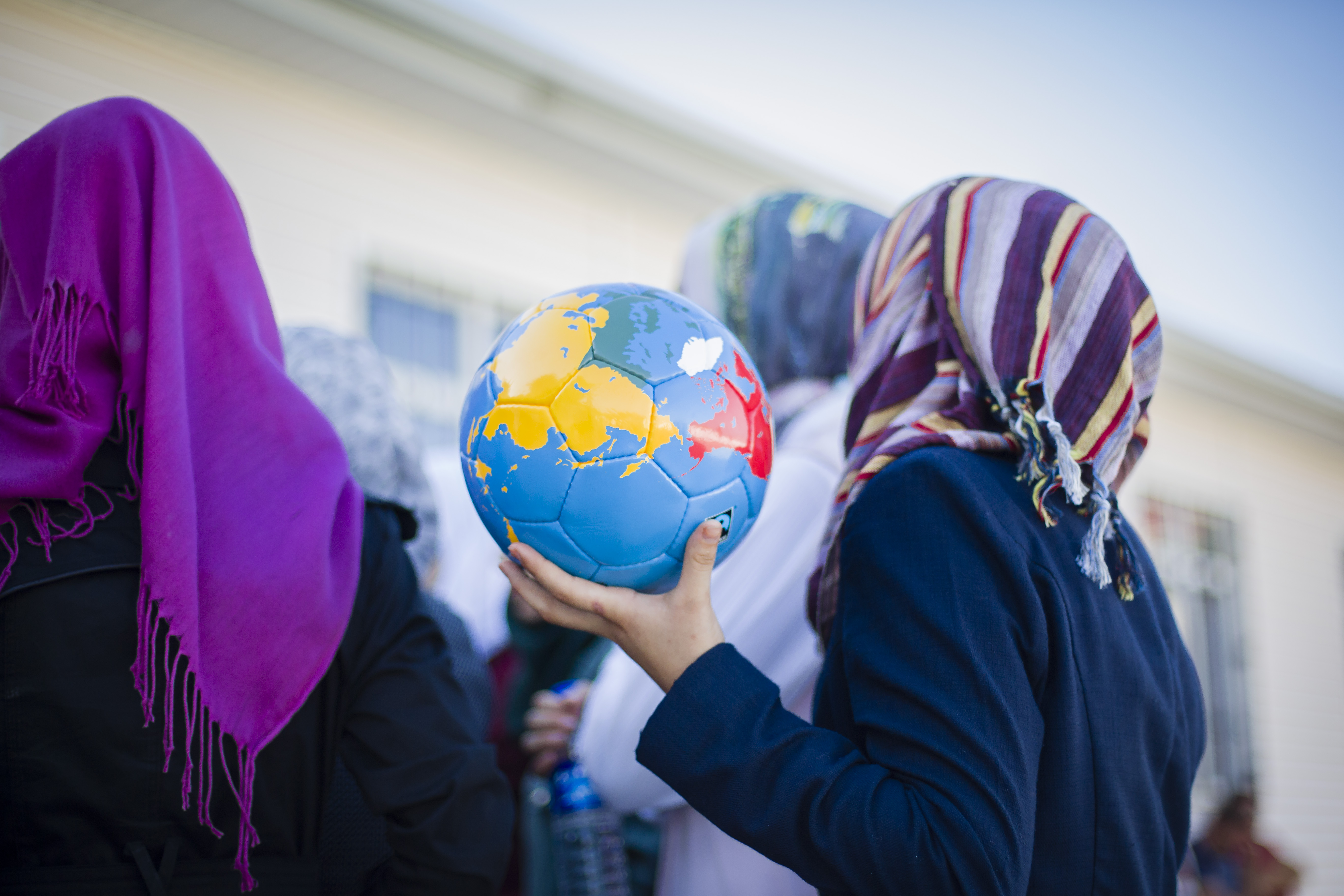 Symbolbild: Migration und Gender, Frauen halten einen Fußball, auf den eine Weltkarte gedruckt ist