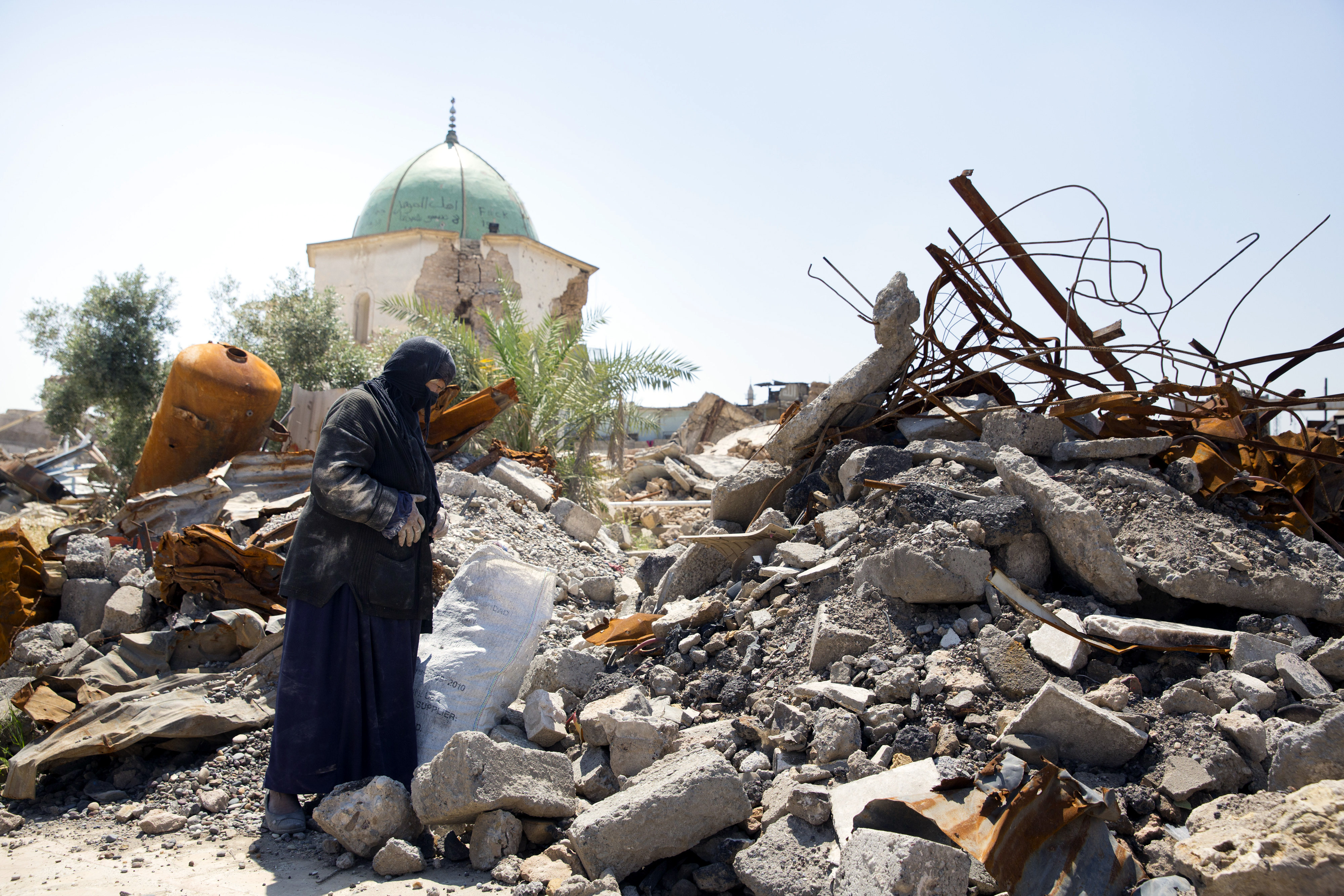 Eine Frau steht in der zer­stör­ten Alt­stadt von Mos­sul, Irak, vor den Trümmern eines Hauses.
