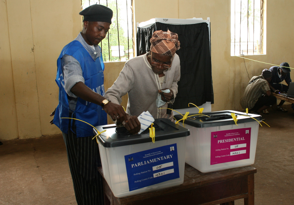 Ei­ne Frau in Si­er­ra Leo­ne wird von ei­nem Wahl­hel­fer bei der Stimm­ab­ga­be un­ter­stützt.