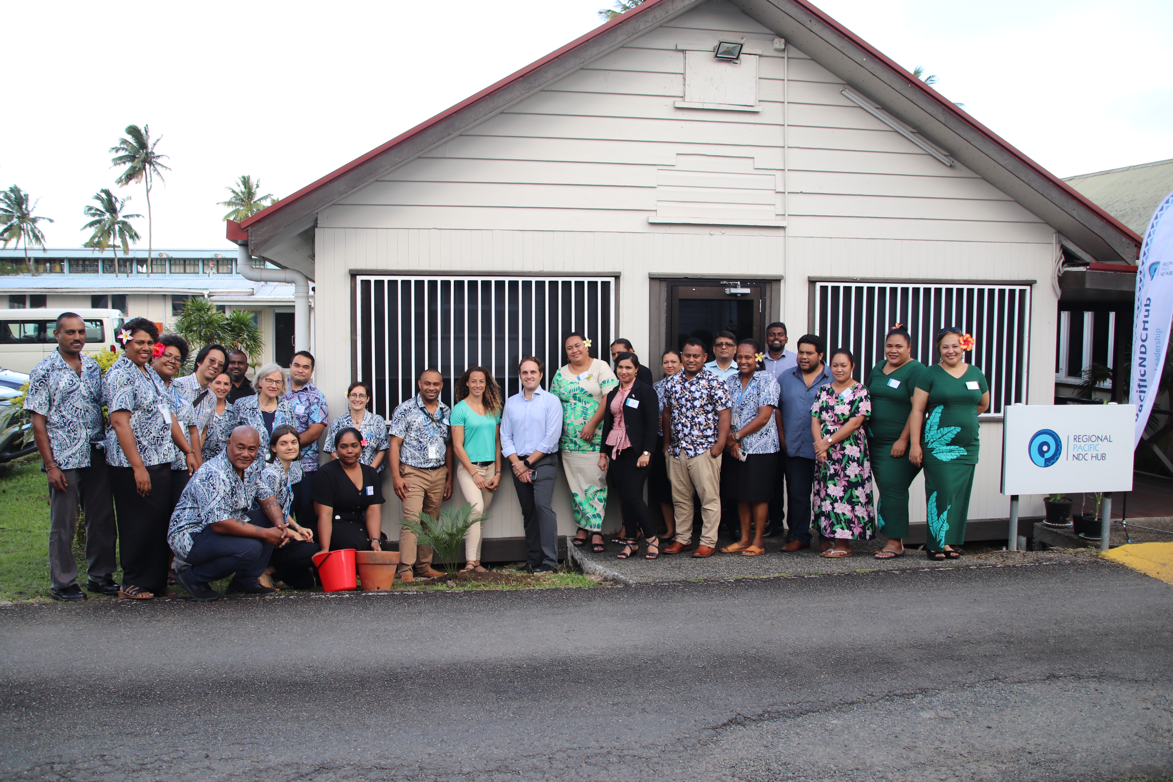 Teilnehmerinnen und Teilnehmer des jährlichen Focal Point Meetings des Regional Pacific NDC Hub pflanzen einen Baum vor dem Büro des NDC Hub.