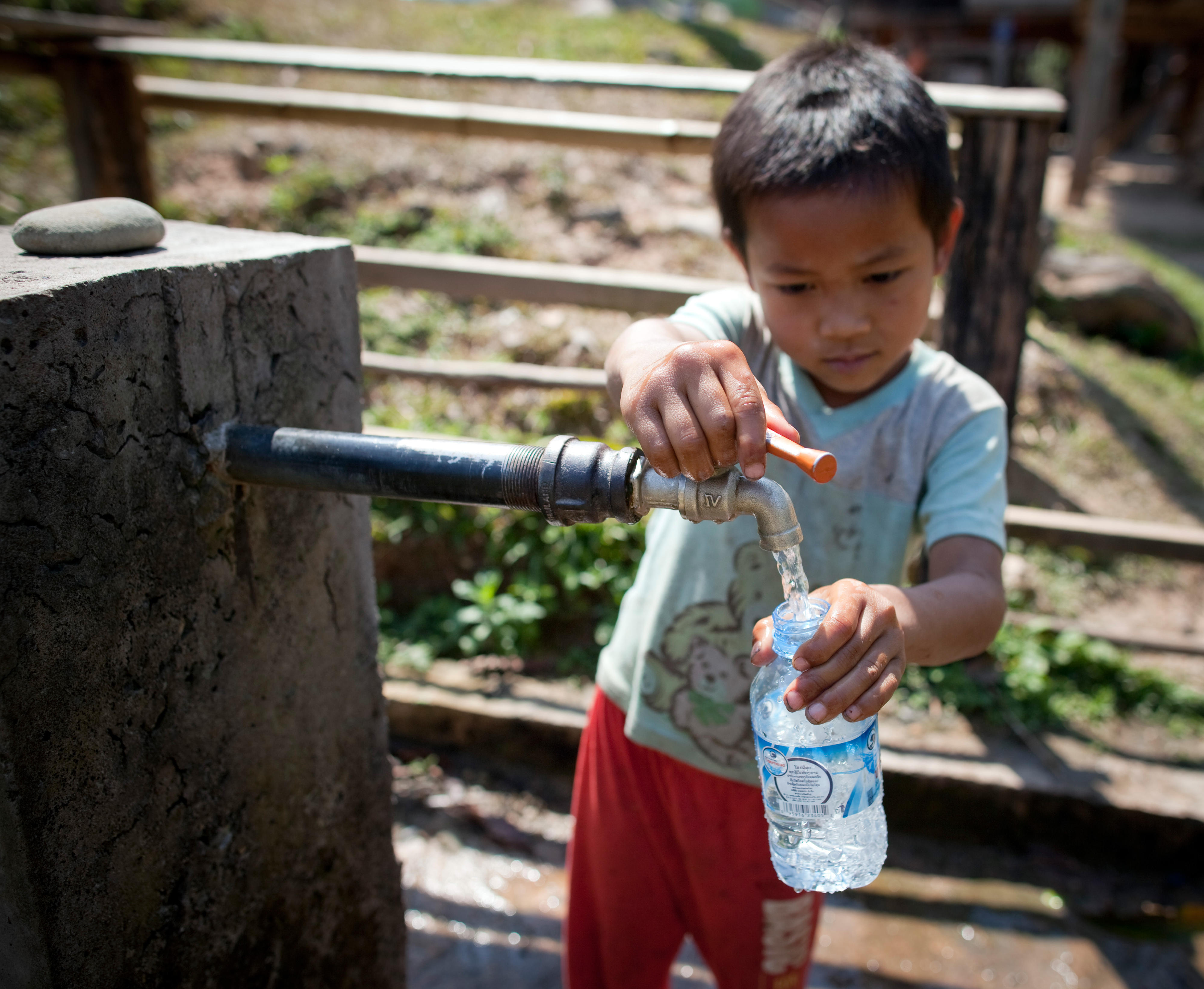 Ein Kind in Vieng Phouka, Laos, befüllt an einem öffentlichen Brunnen eine Flasche.