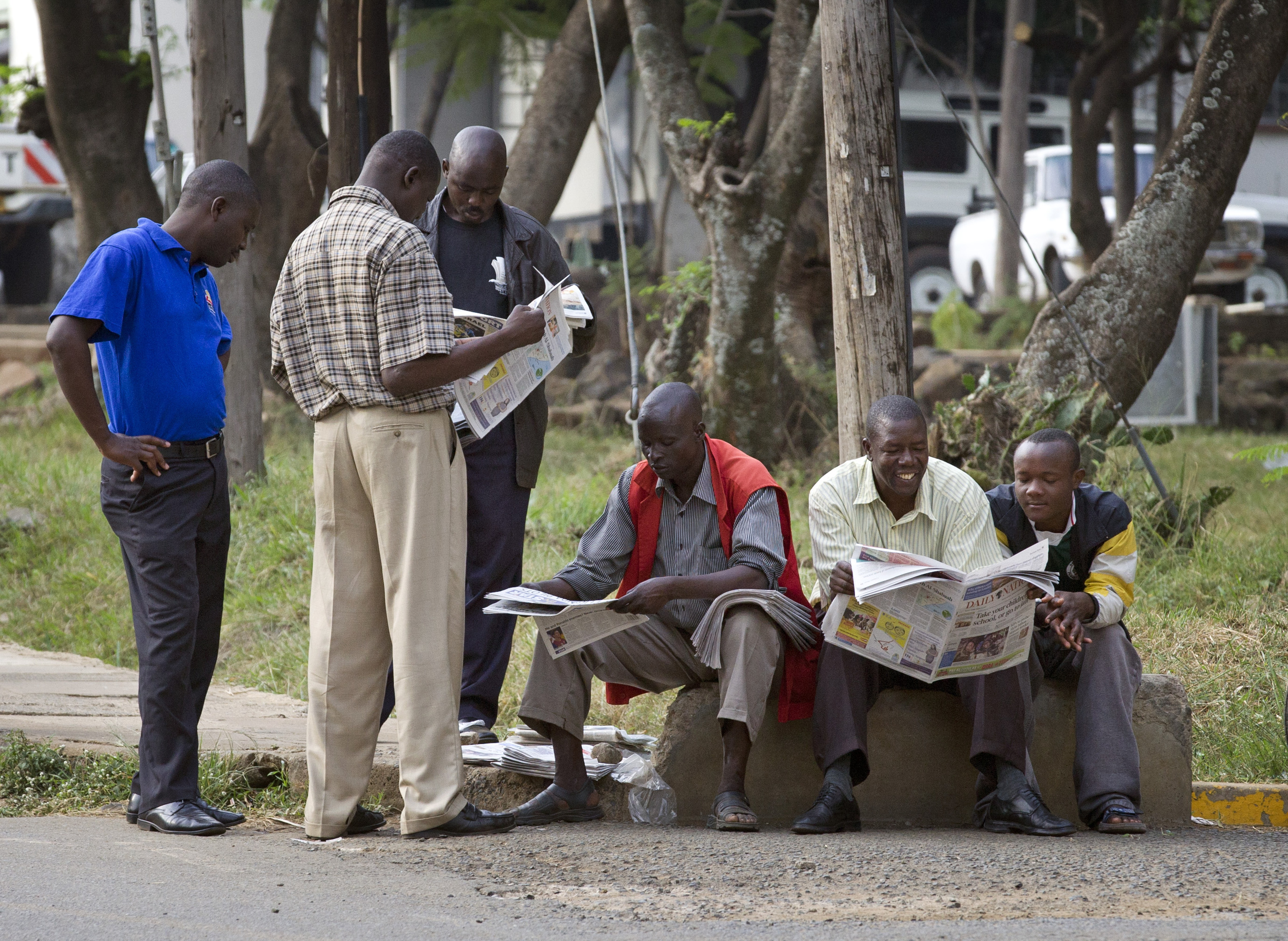 Kenya: Men reading newspapers on the side of the road.