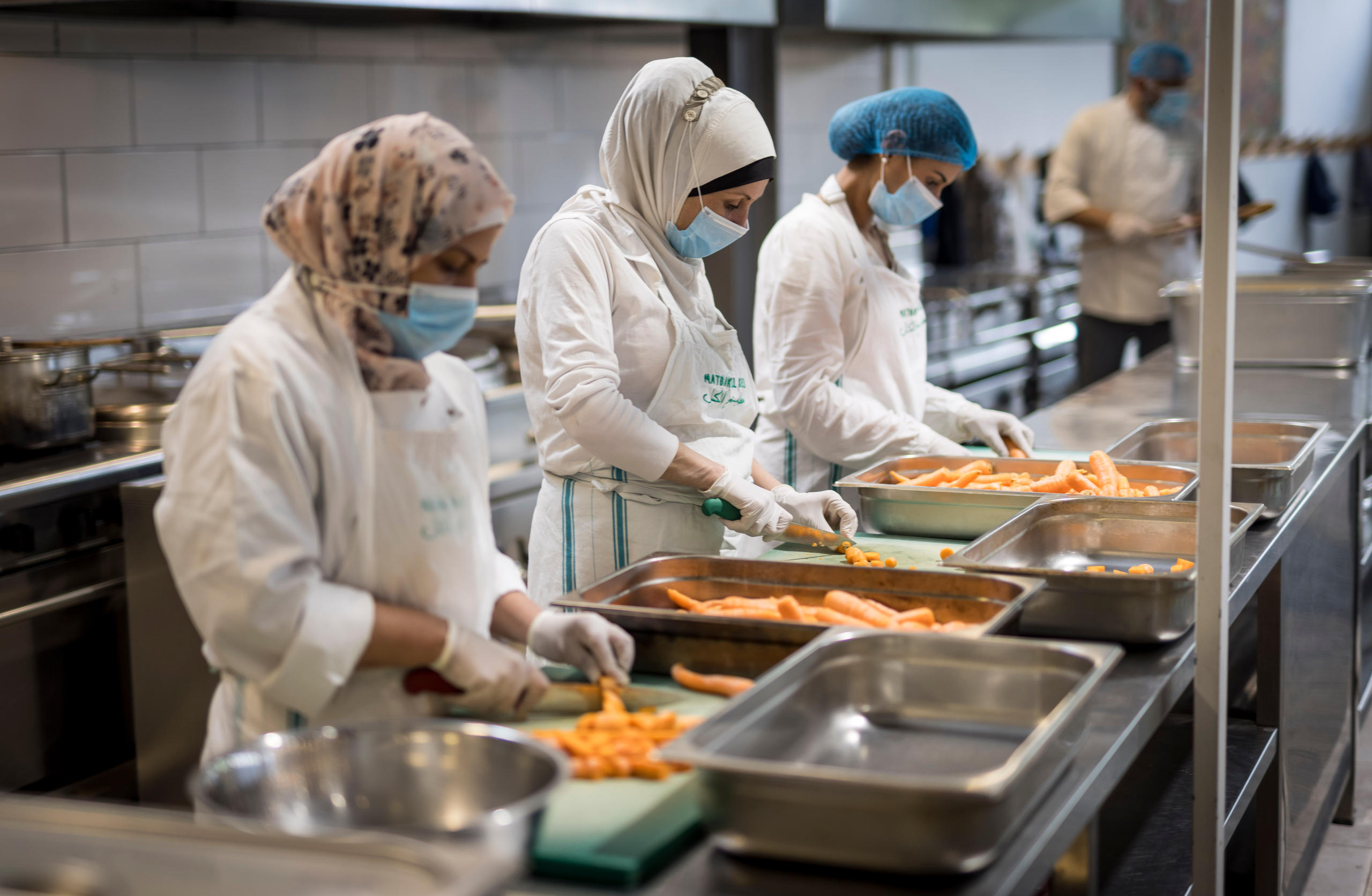 Foto von Frauen, die in einer Industrieküche Gemüse schneiden.