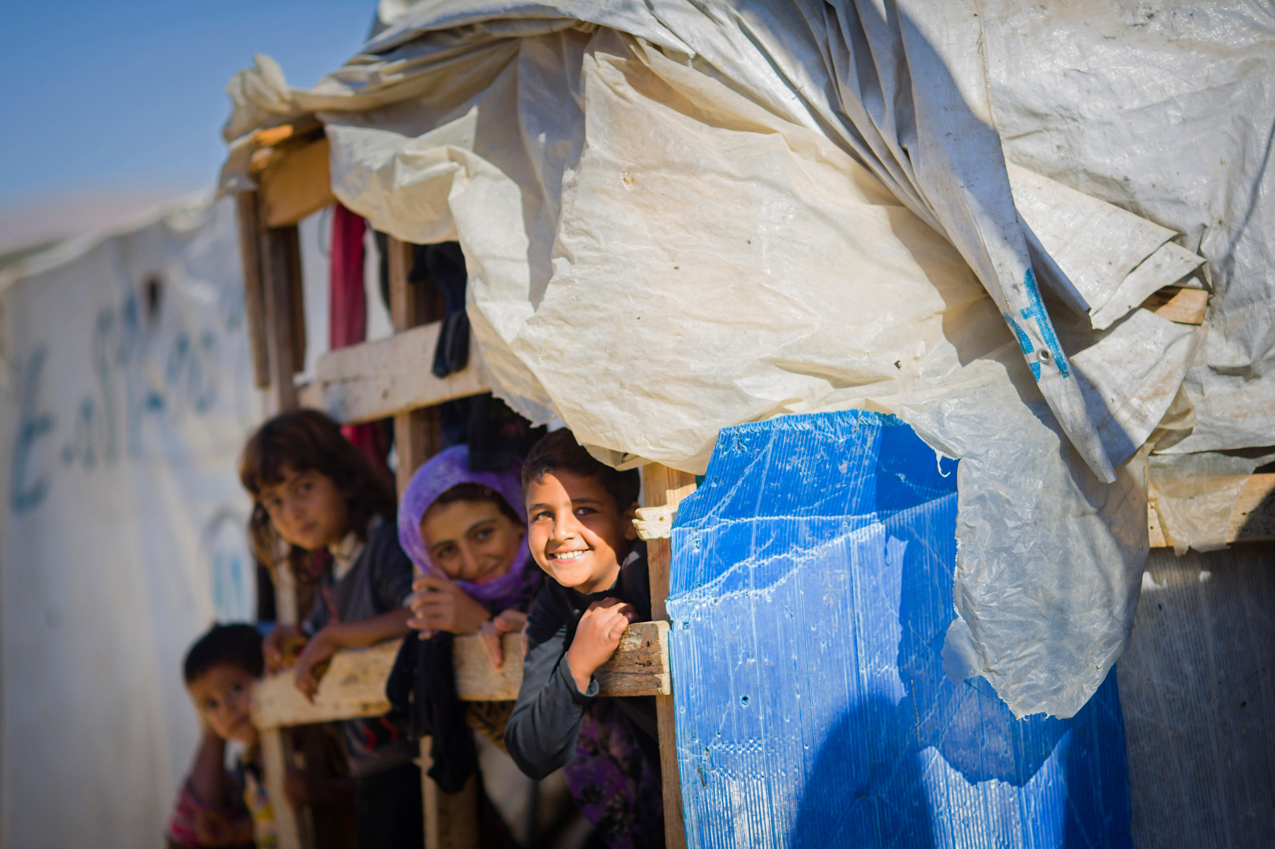 Syrian children are looking out of a tent in a refugee camp in the Bekaa Valley.