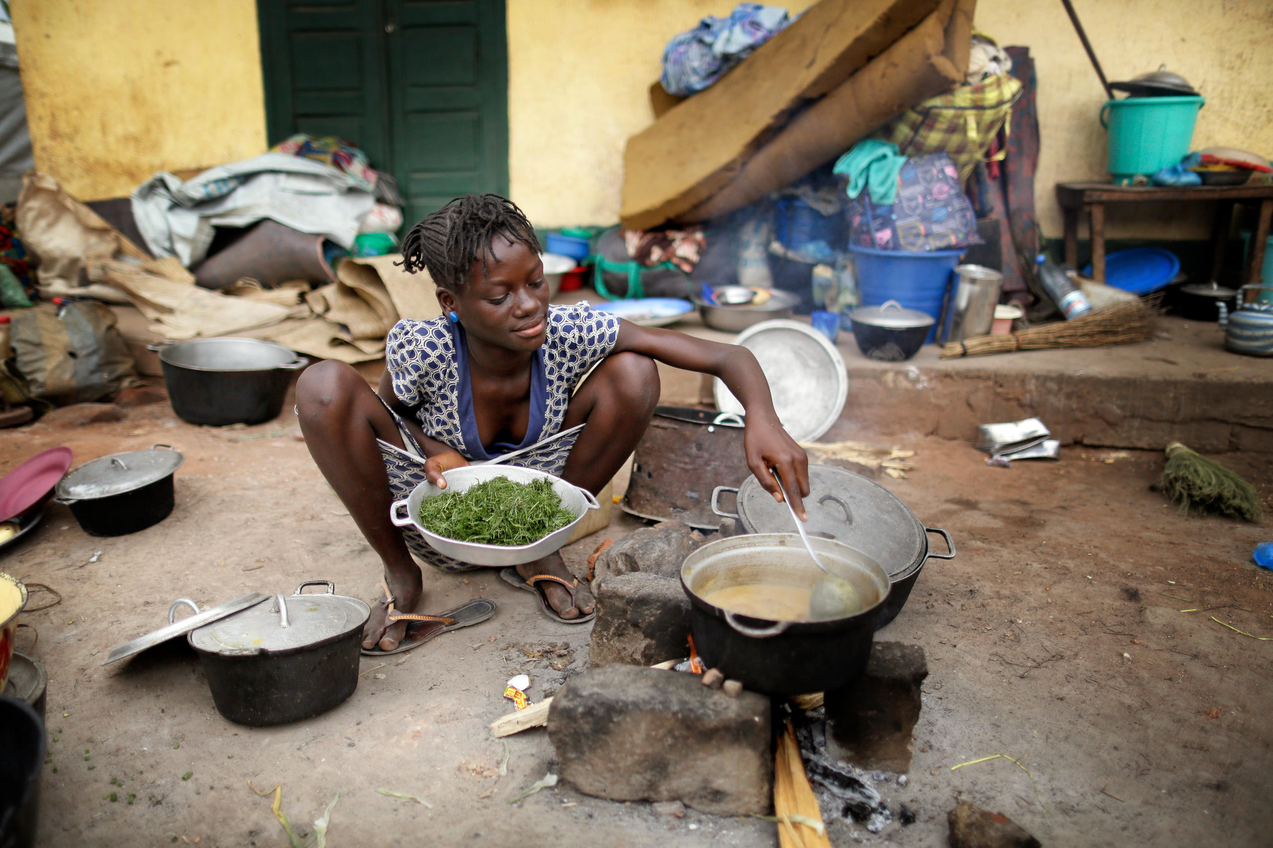 Eine junge Frau kniet in der Hocke und kocht über offenem Feuer 