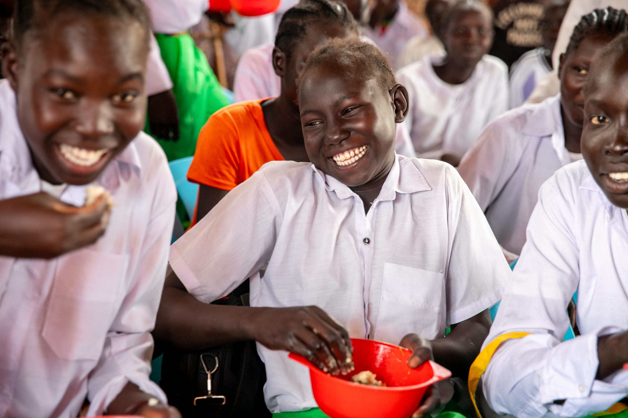 Drei Mädchen in Schulinform im Südsudan essen lachend ihr Mittagessen