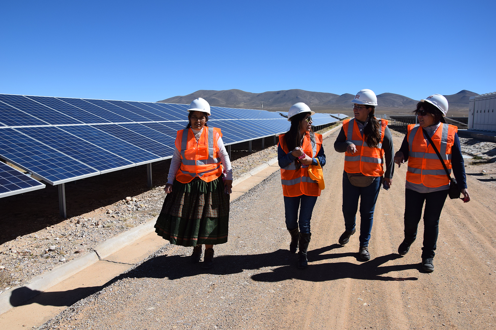 Foto von vier Frauen, die neben einer Photovoltaikanlage lang laufen.
