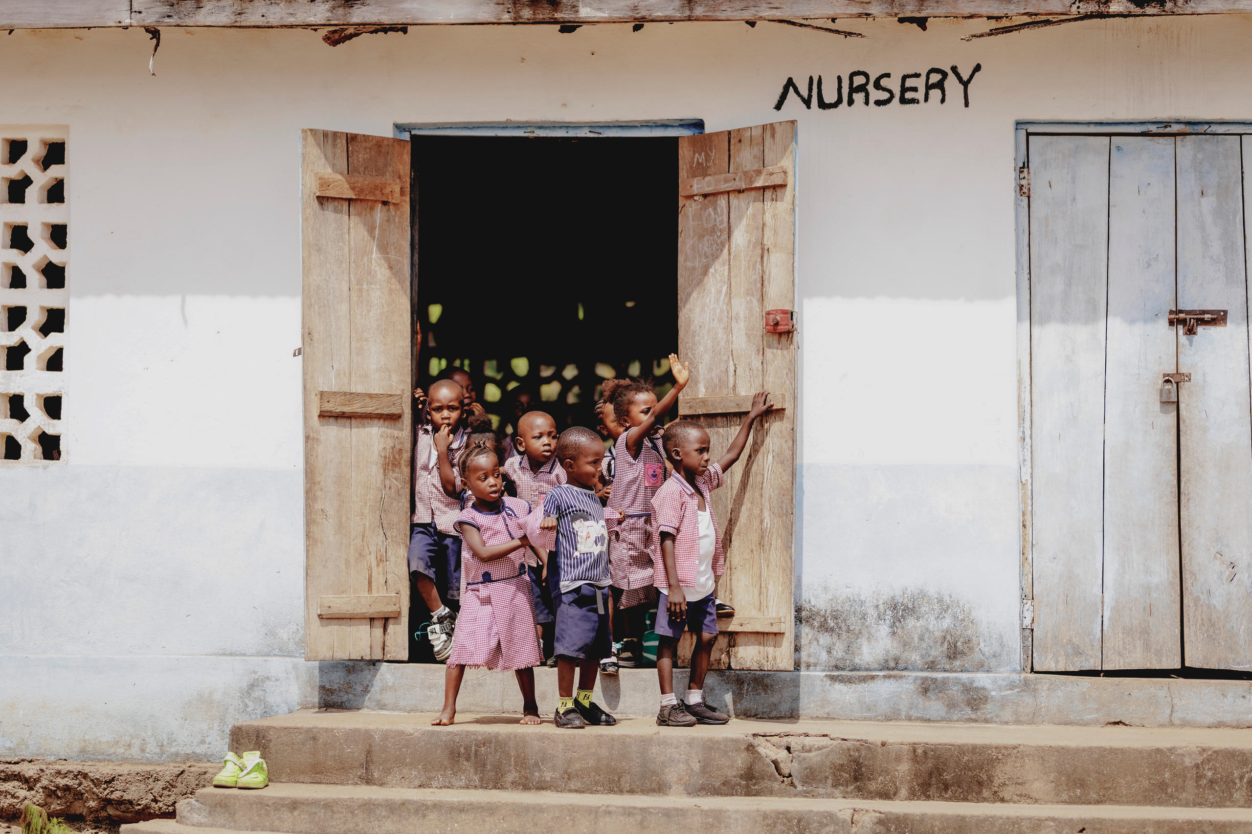 Schulkinder in Sierra Leone winken aus einer Holztür heraus