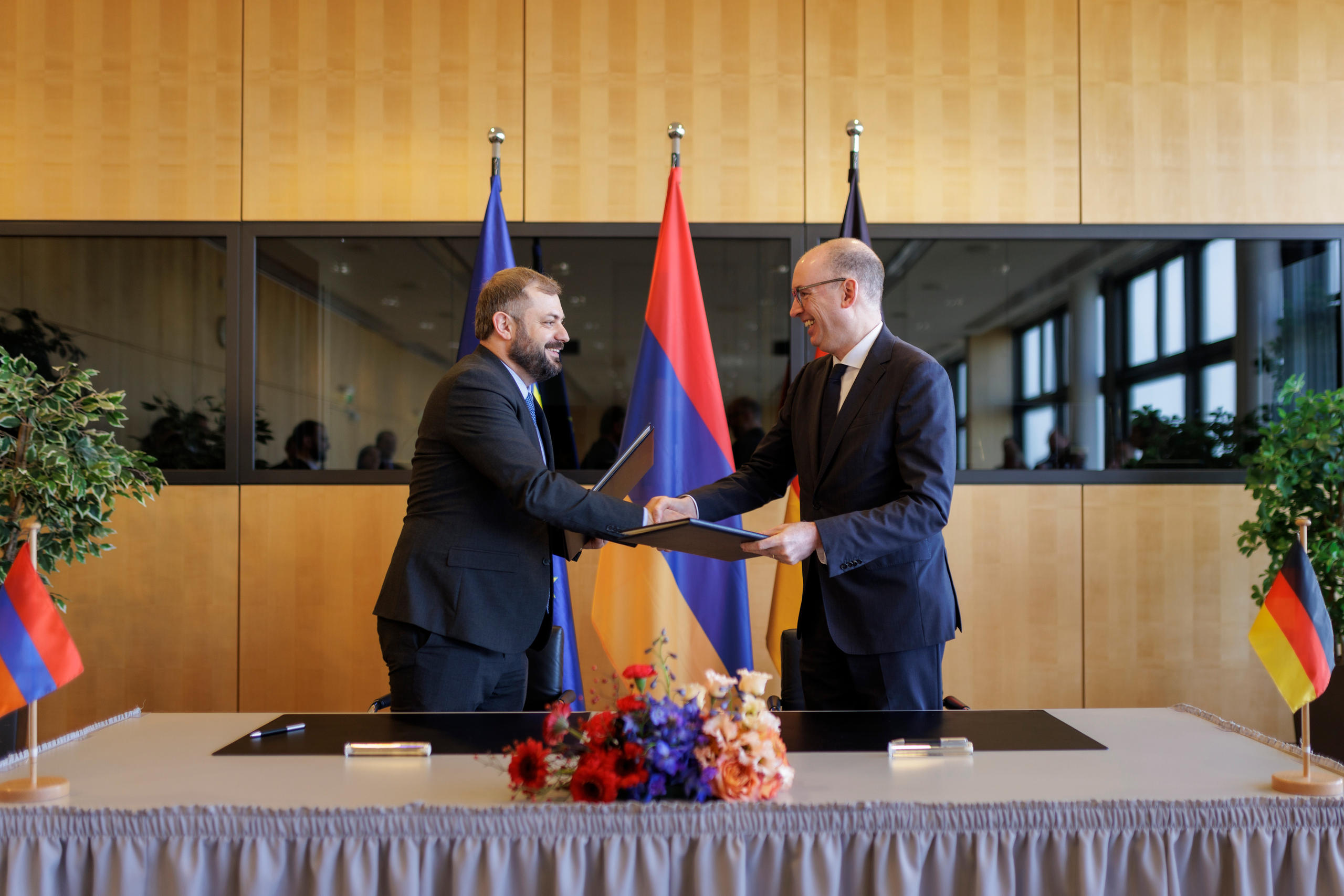 Zwei Männer geben sich vor der armenischen und deutschen Flagge die Hand