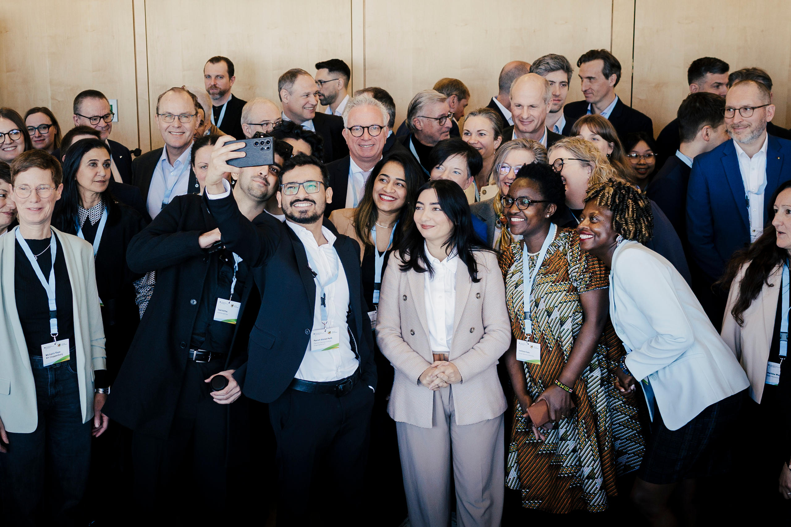 Foto von mehreren Menschen, einer davon macht ein Selfie mit seinem Handy.