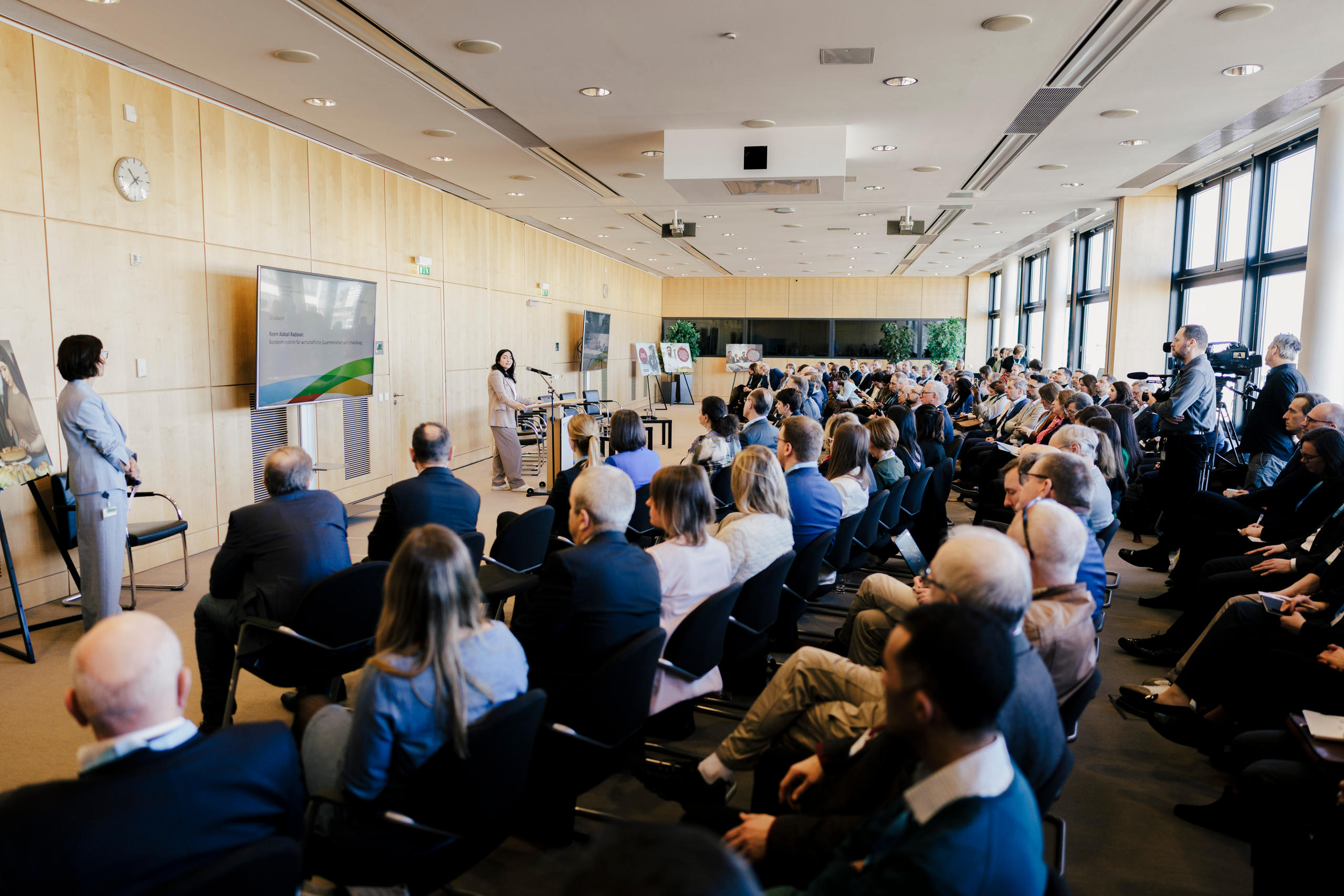 Foto von einer Menge an Menschen, die einer Präsentation auf einem Bildschirm folgen.