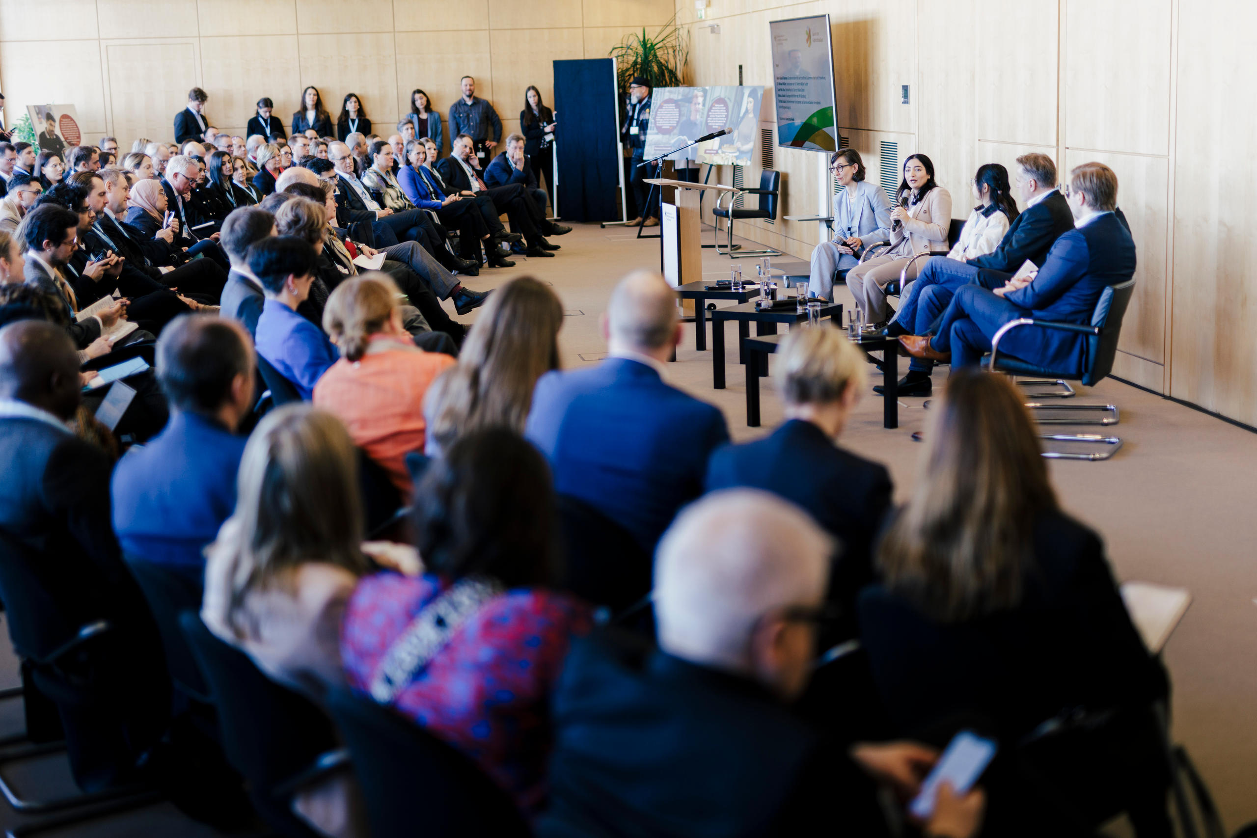 Foto von fünf Menschen, die vor einer großen Anzahl von Menschen sprechen.