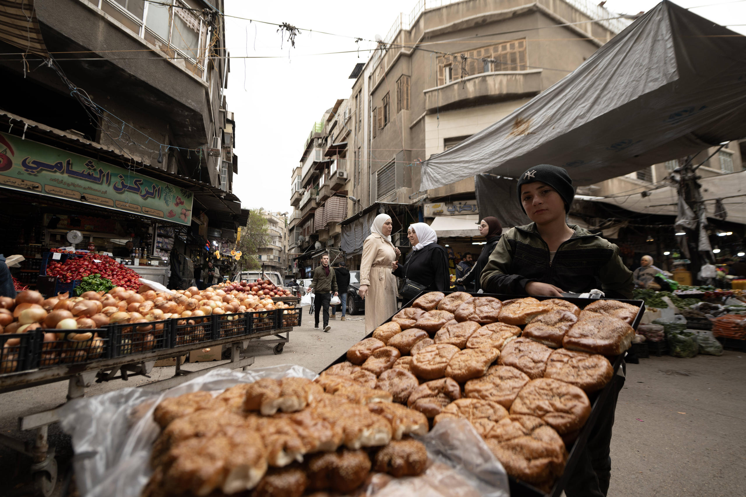 Photo of a boy selling bread at a market on a street between houses.