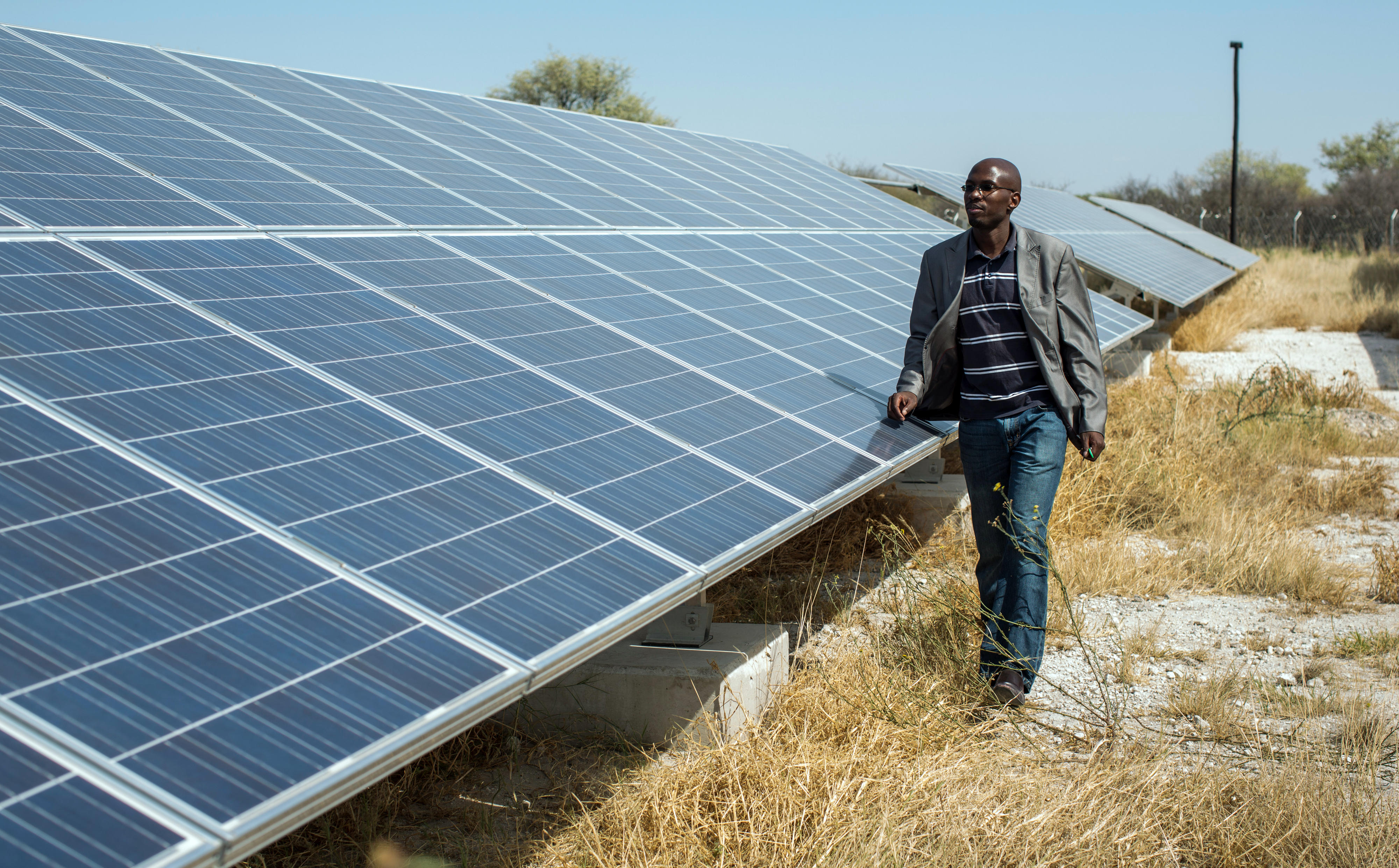 A man stands in front of a solar power plant in Namibia, which consists of numerous panels.