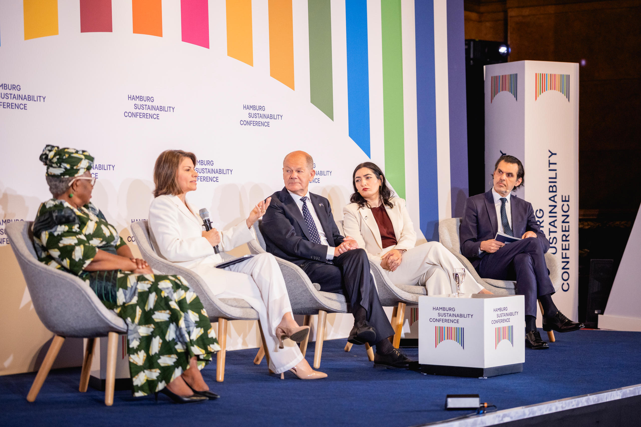 Foto von fünf Menschen, die auf einem Podium nebeneinander Sitzen. Eine Frau davon spricht in ein Mikrofon.