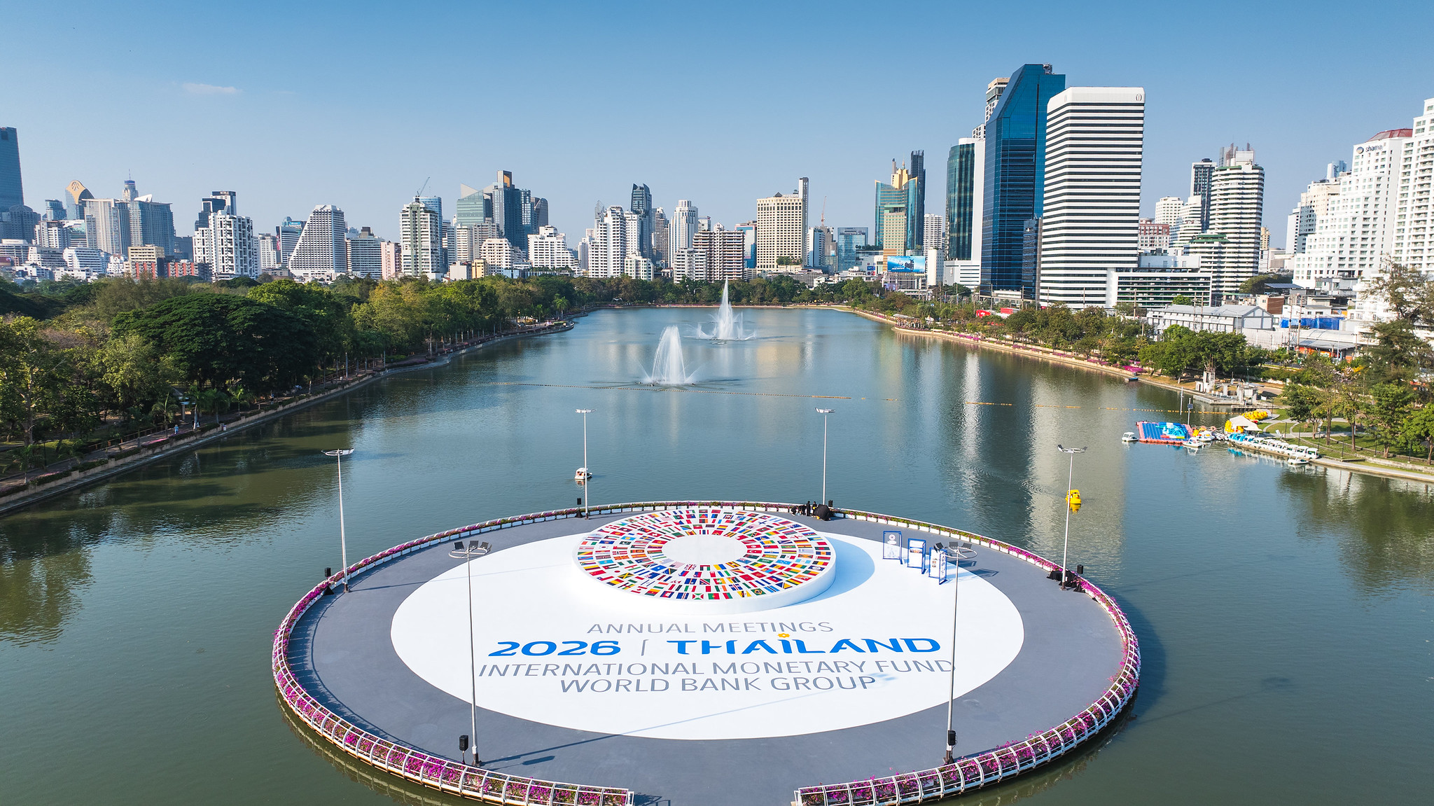 Blick auf einen großen See in einer Stadt mit Springbrunnen und einer runden Plattform mit dem Schriftzug '2023 ANNUAL MEETINGS THAILAND INTERNATIONAL MONETARY FUND WORLD BANK GROUP'.