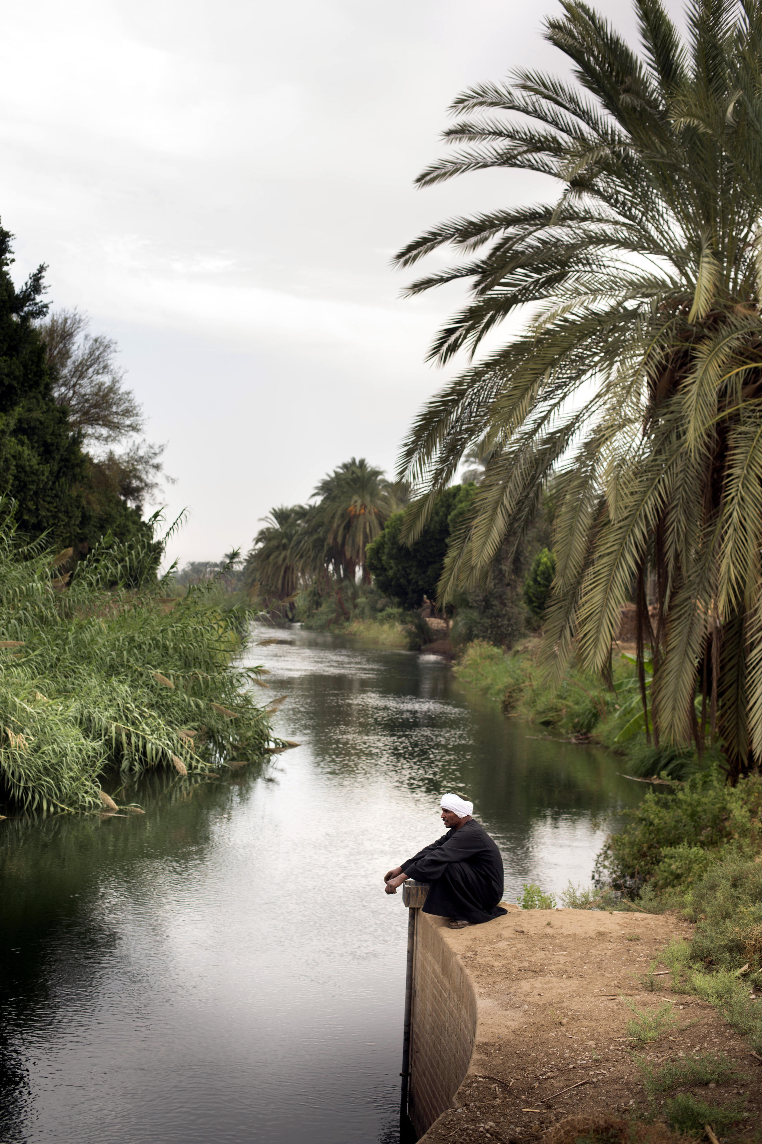 Ein Mann sitzt an einem Bewässerungskanal in der Nähe von Qena am Nil, Ägypten. 