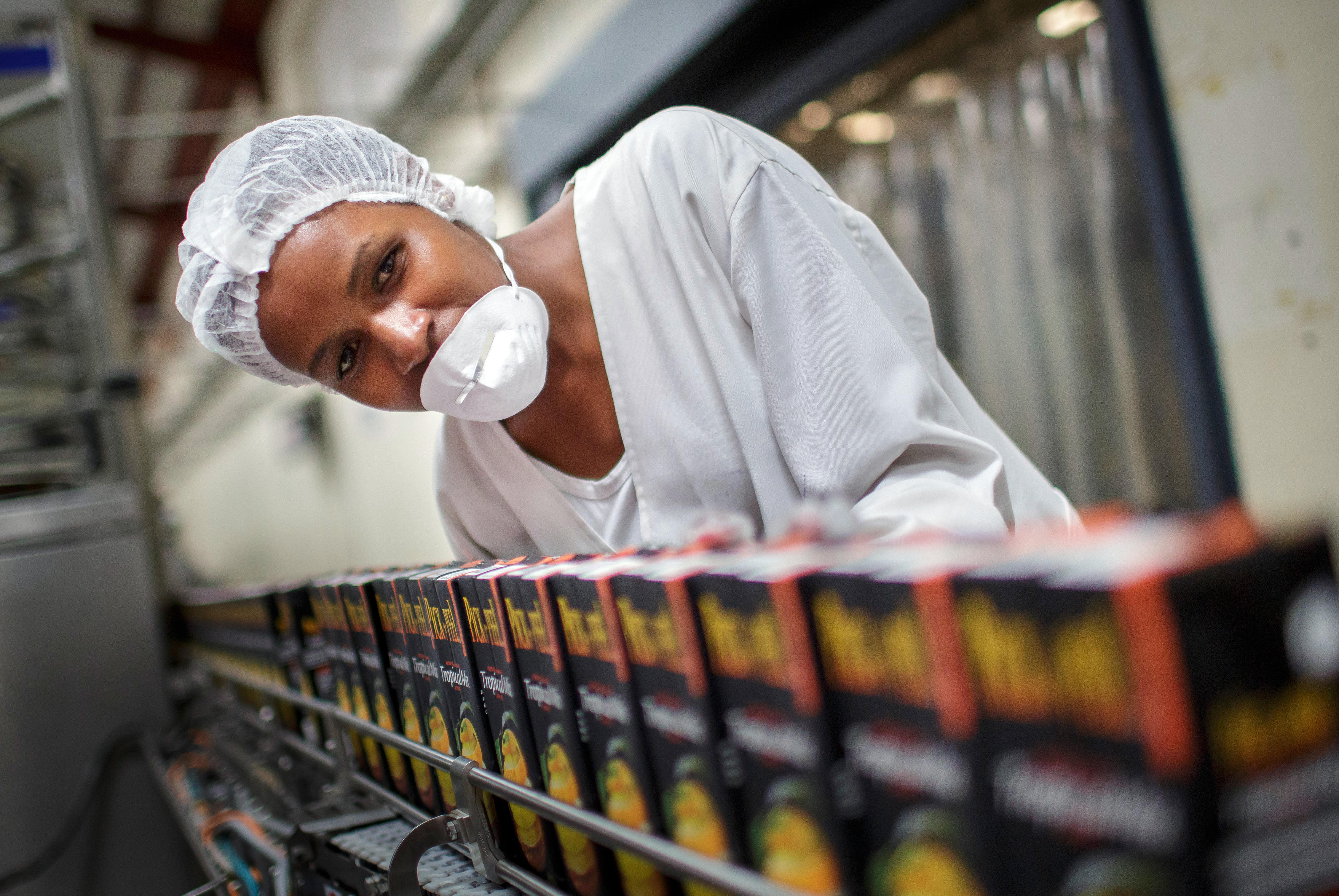 Eine Mitarbeiterin kontrolliert ein Fließband, auf dem Tetrapacks mit Fruchtsaft befördert werden.