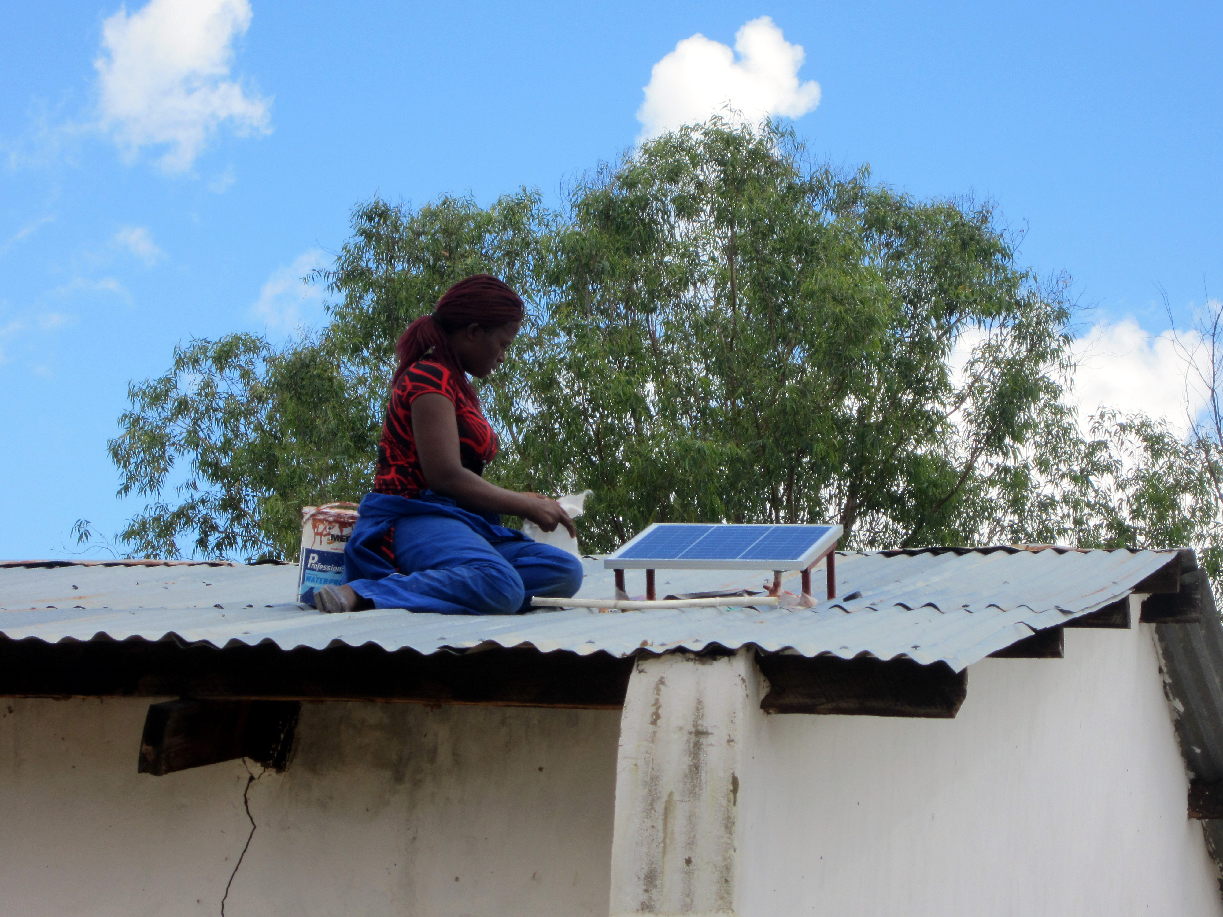 Eine Frau in Malawi montiert eine kleine Solaranlage auf das Dach ihres Hauses.