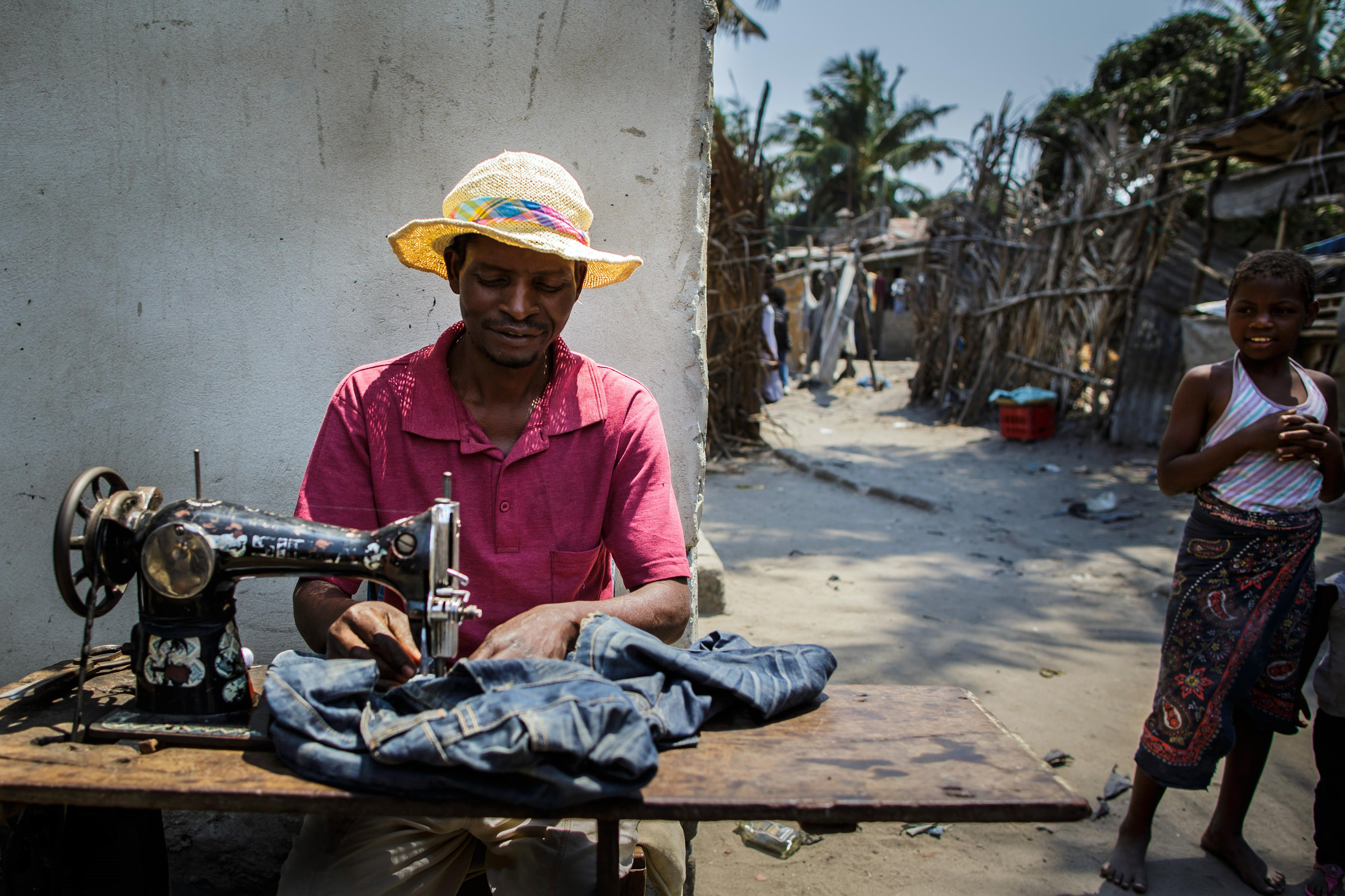 Ein Schneider arbeitet in einem Armenviertel der mosambikanischen Stadt Beira mit seiner Nähmaschine auf der Straße.