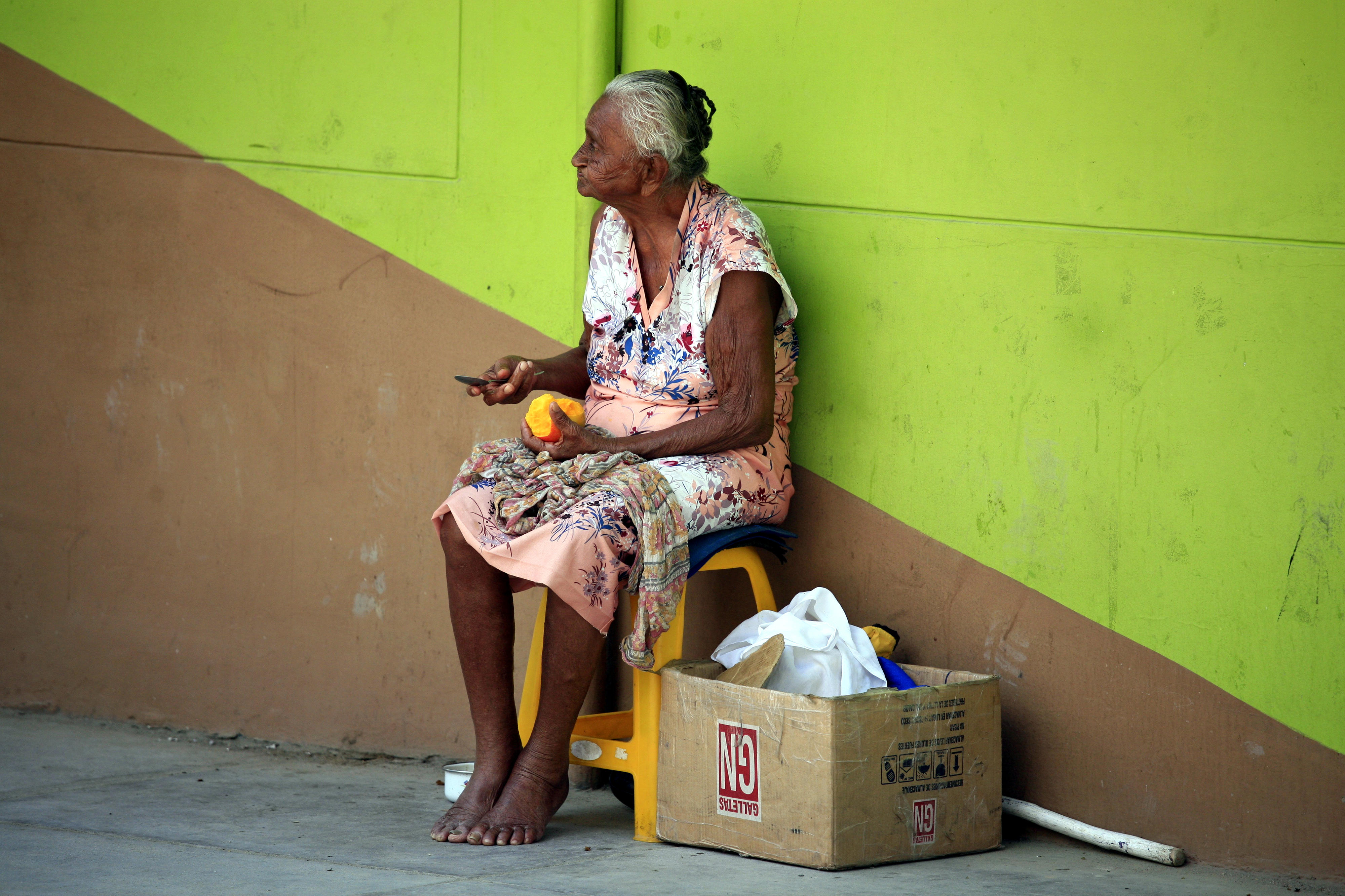 An older woman peeling a mango by the side of a street