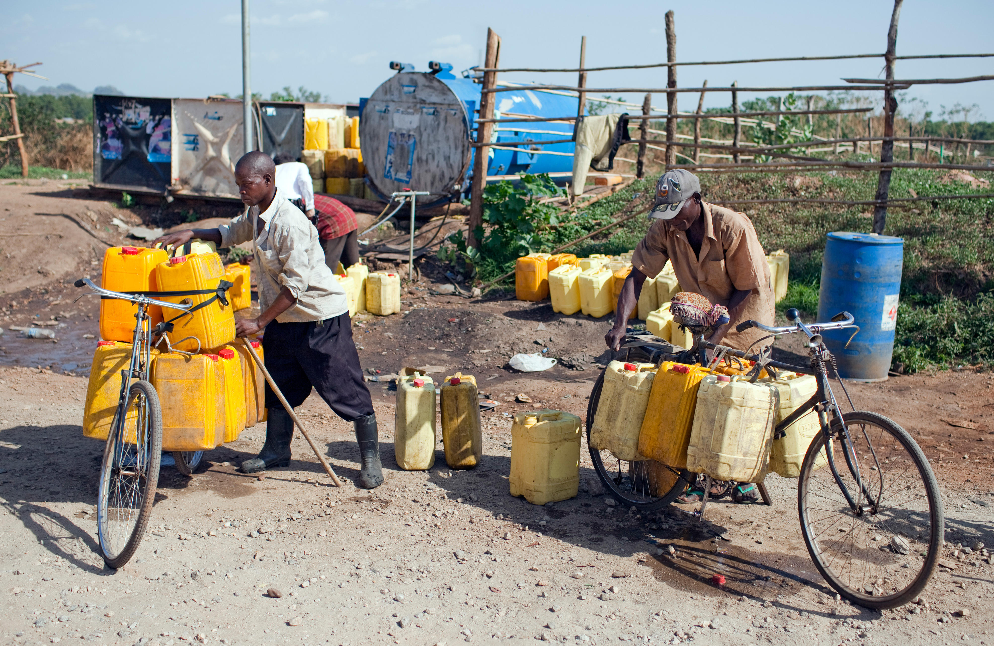 Two men fetch water from a public well with a bicycle.