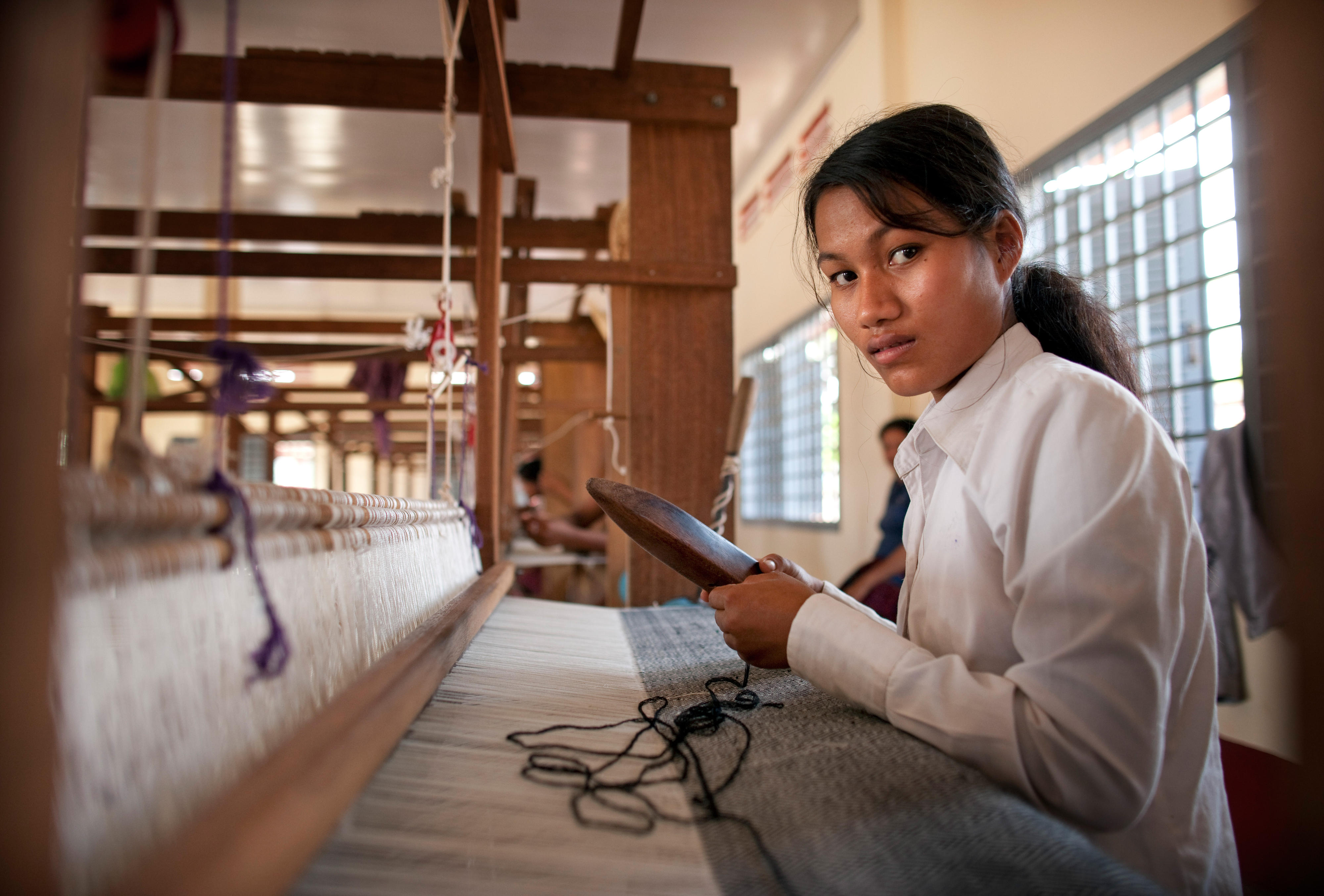 A woman learns to operate a loom.