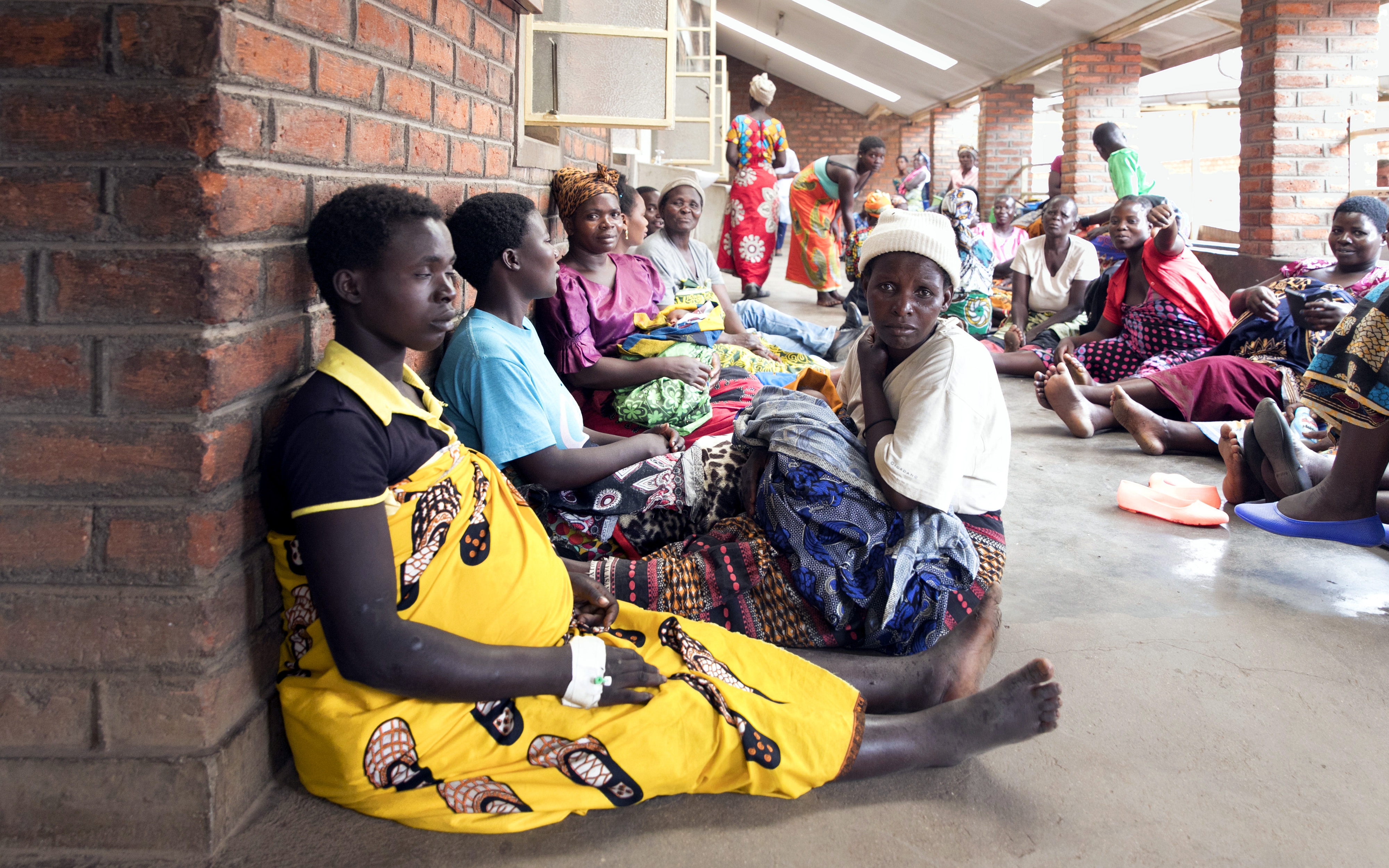 Wartende Patientinnen in der Geburtsstation des Nkhoma-Krankenhauses in Malawi. Zahlreiche Frauen, manche von ihnen sichtbar schwanger, sitzen auf dem Boden einer langgestreckten Veranda. 