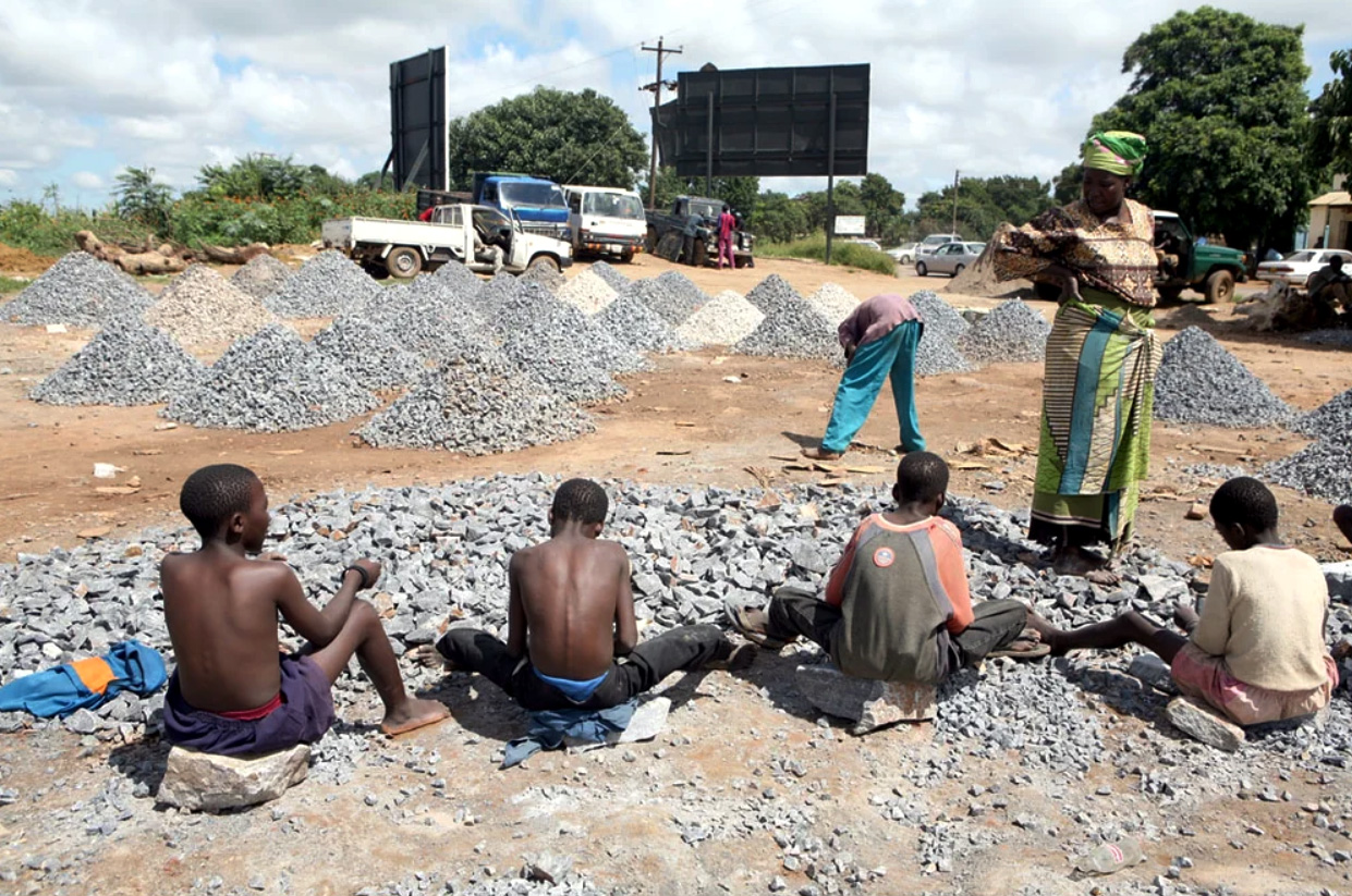 Kinderarbeit in einem Steinbruch in Sambia sitzen vier Jungen und bearbeiten Steine