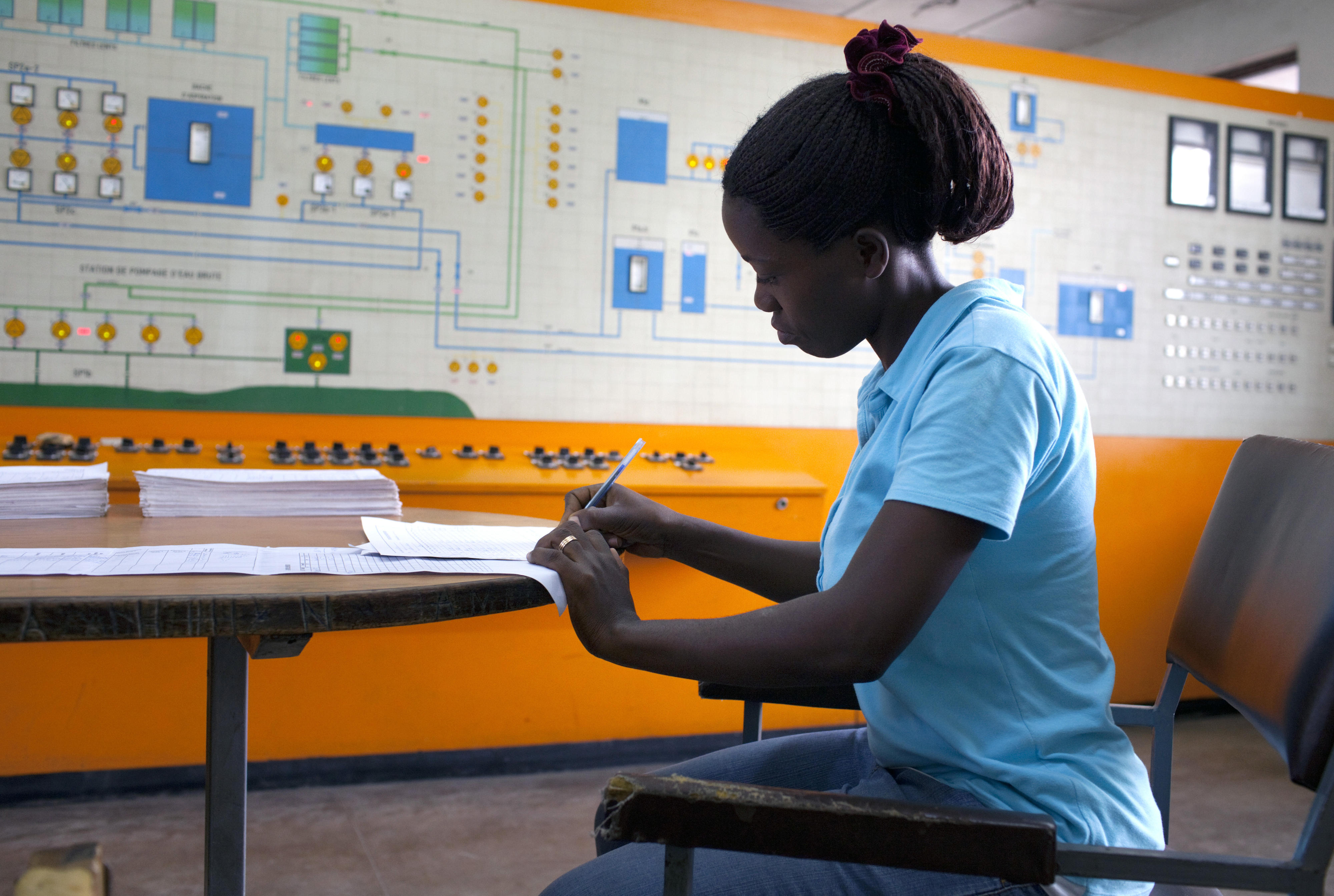 Eine technische Angestellte in der Schaltzentrale der Pumpstation eines Wasserprojekts der KfW Entwicklungsbank in Bujumbura in Burundi sitzt an einem Tisch und schreibt mit einem Kugelschreiber in ein Formular.