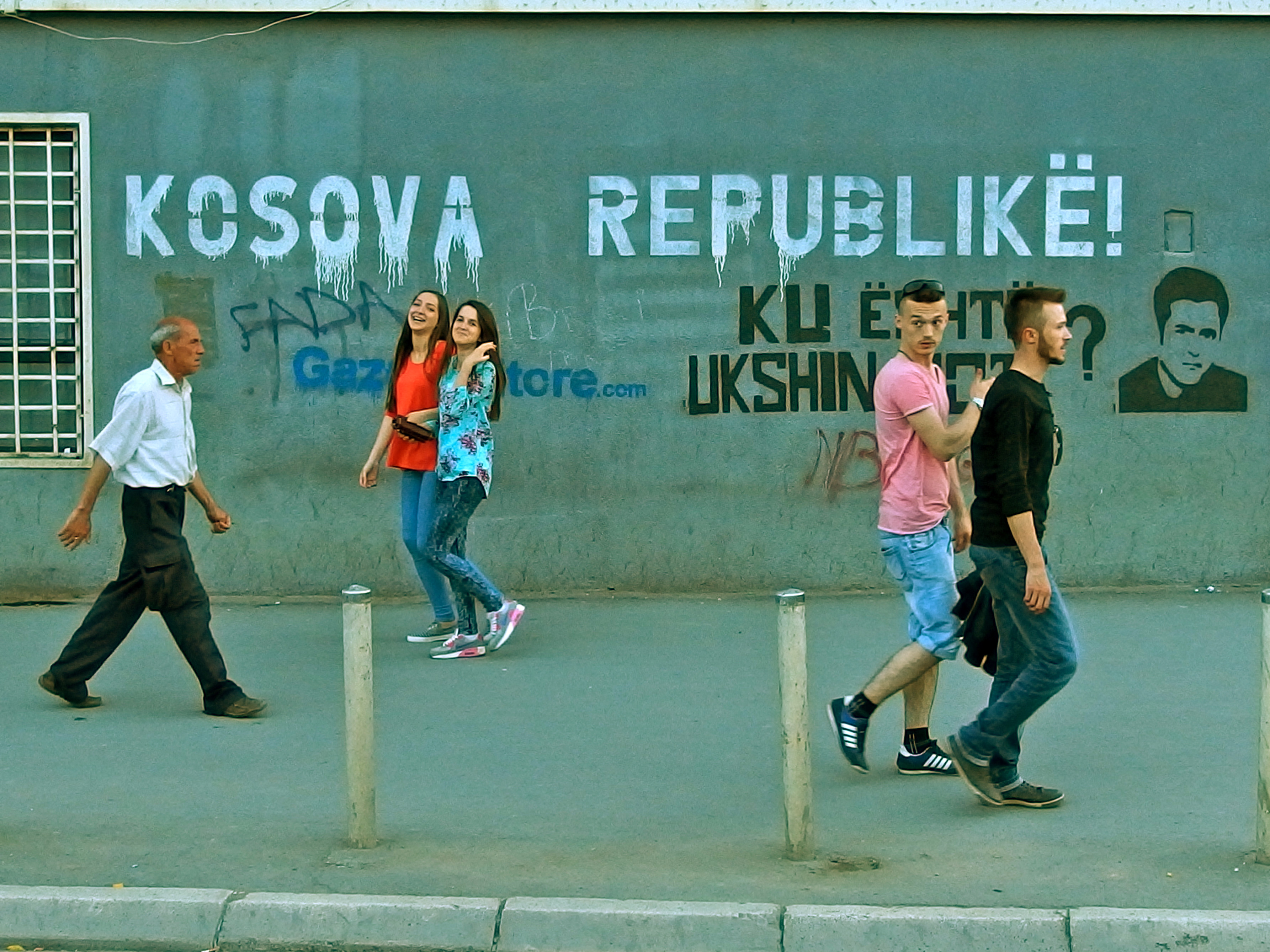 People on a pavement in Pristina, the capital of Kosovo, in the background you can see graffiti.