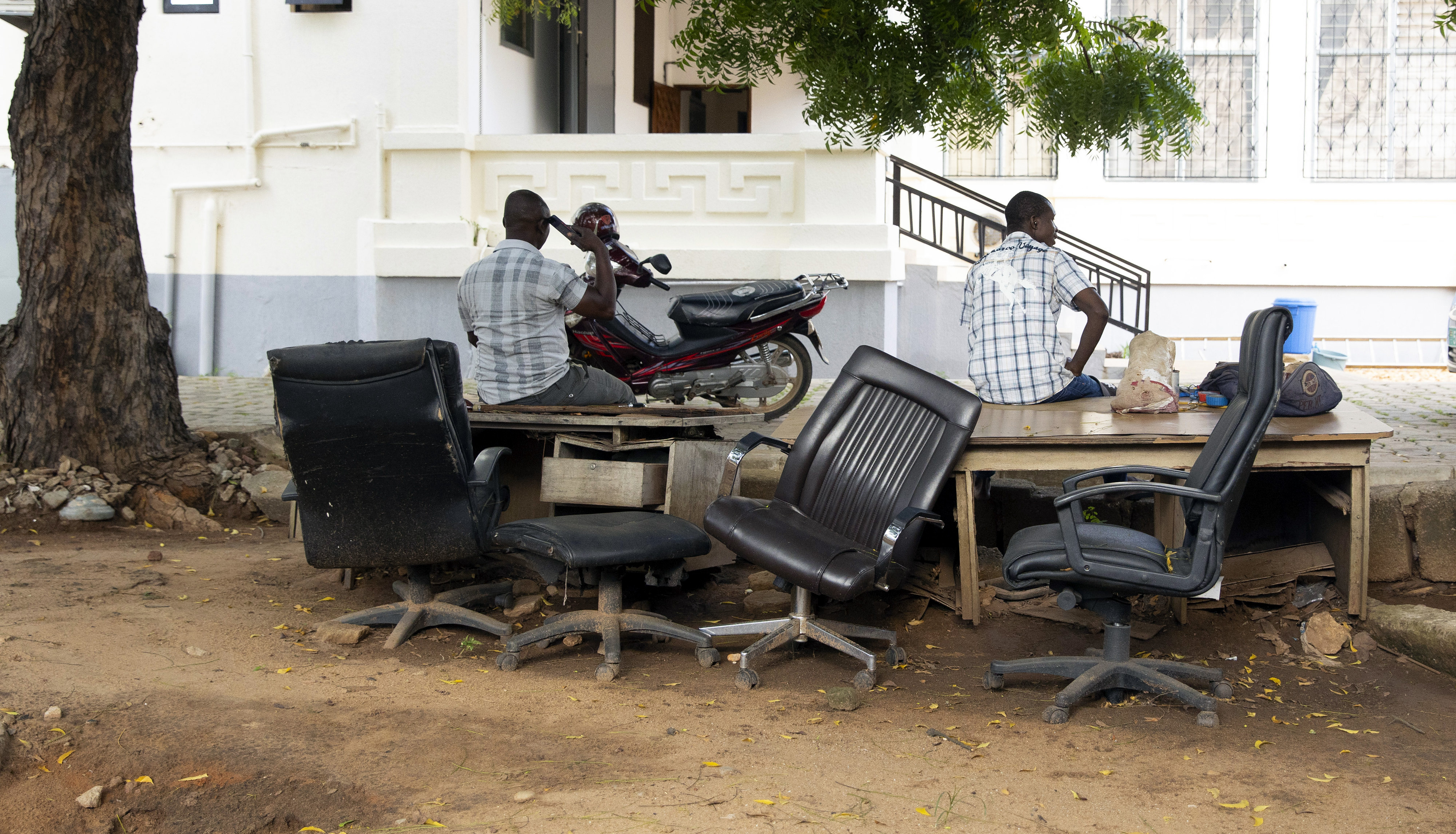 Straßenszene in Togo: Zwei Männer sitzen am Straßenrand auf alten Tischen