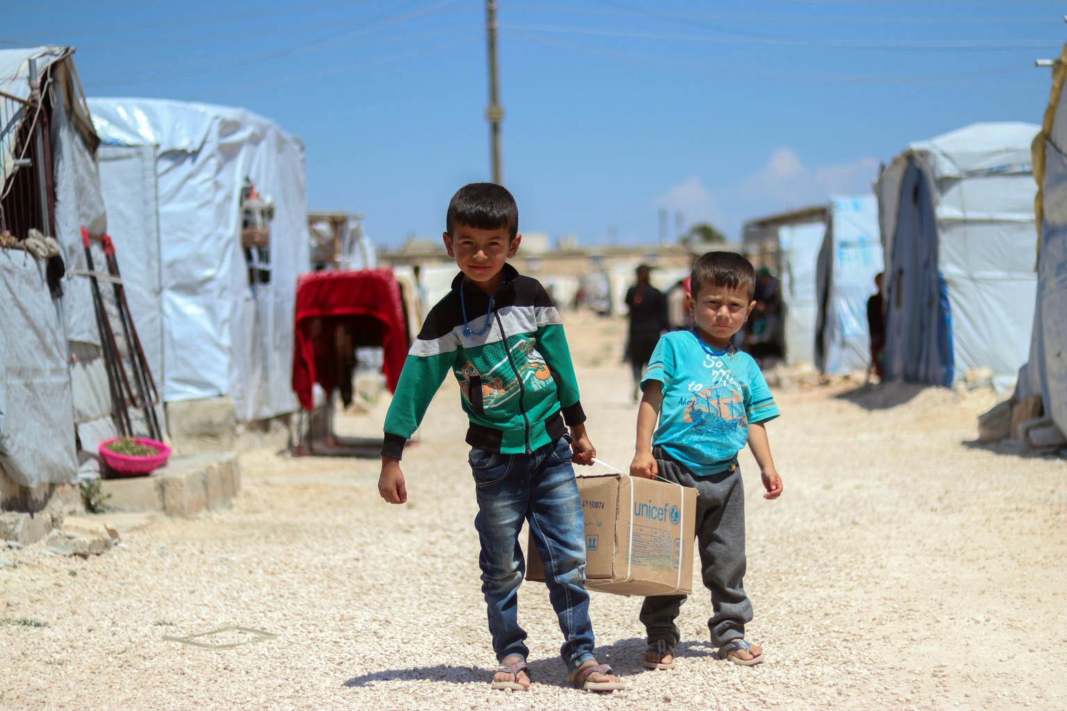 Two children carry a family hygiene package from UNICEF to their tent in Fafin camp near Aleppo.