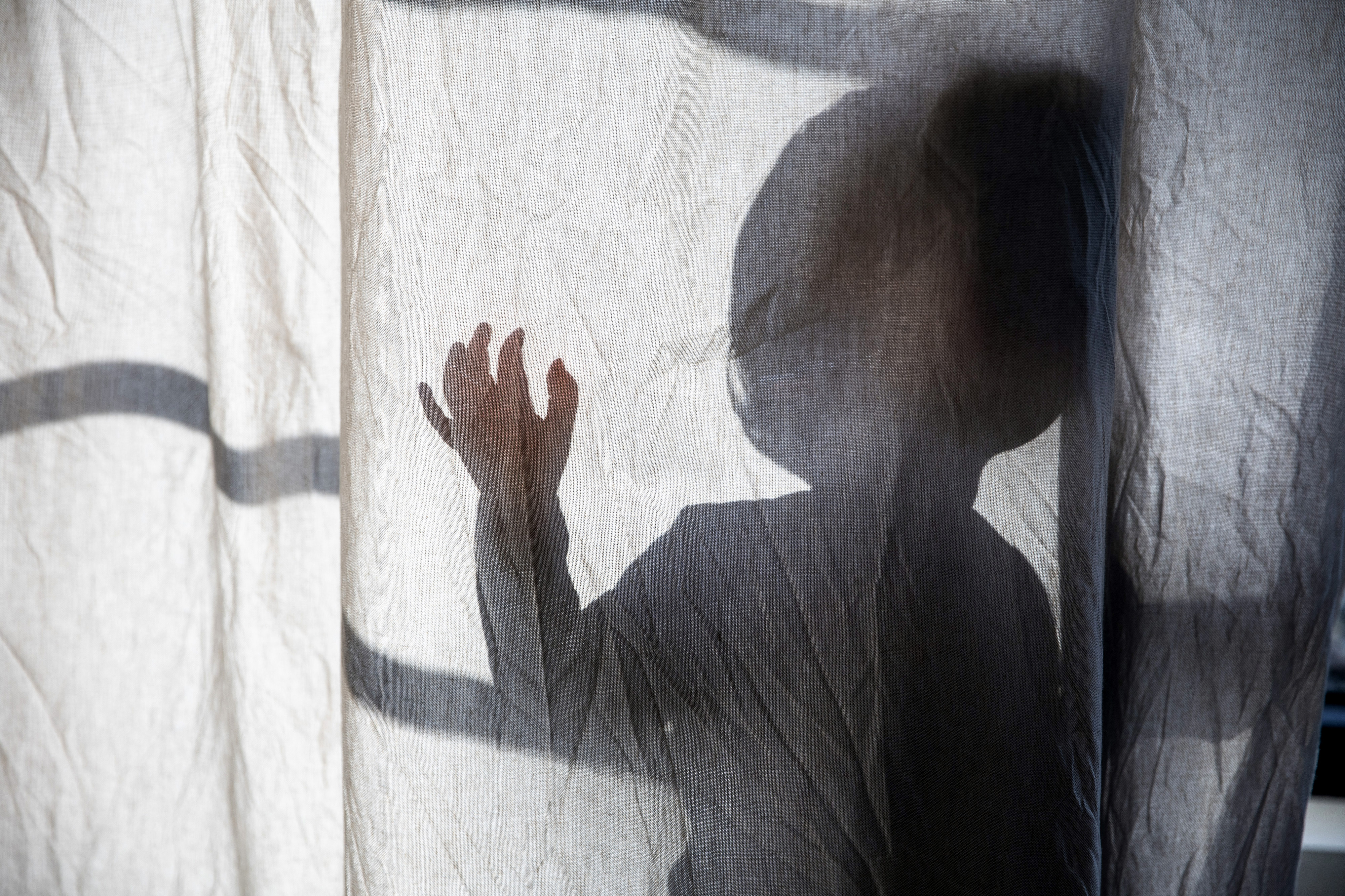 Symbolfoto Trauma: Der Schatten eines Kindes ist hinter einem Vorhang erkennbar